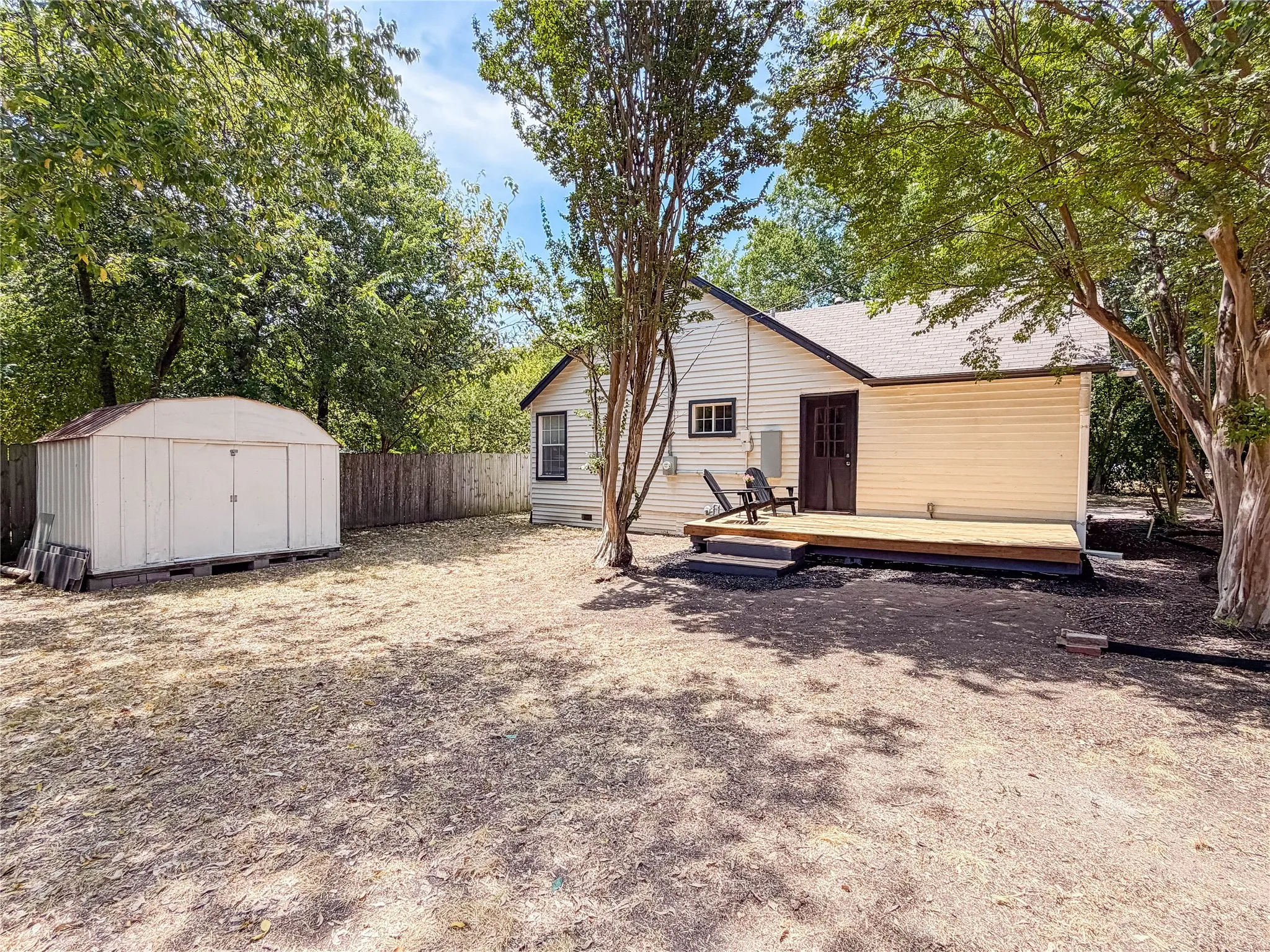 Rear exterior with a wooden deck, wood privacy fence, and a storage shed
