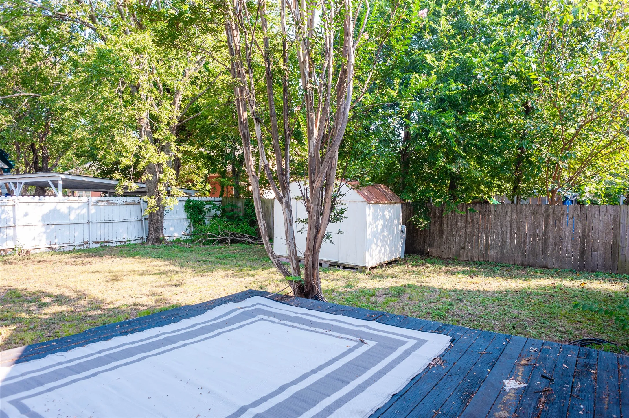 Backyard featuring a wooden deck, mature trees, a storage shed, and perimeter fencing