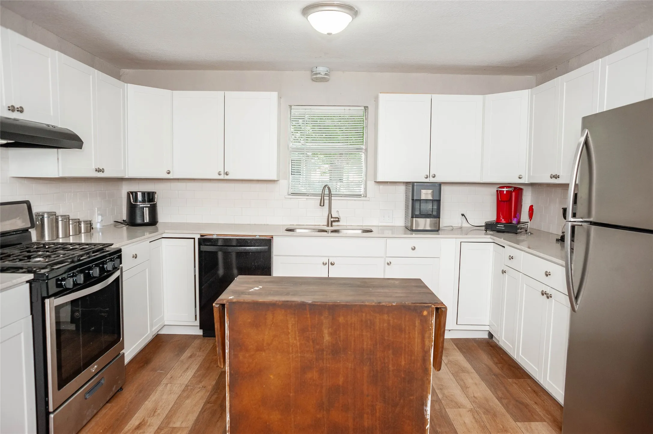 Kitchen featuring white cabinetry, light countertops, wood-finish flooring, stainless steel refrigerator, and a built-in stainless steel range with overhead ventilation
