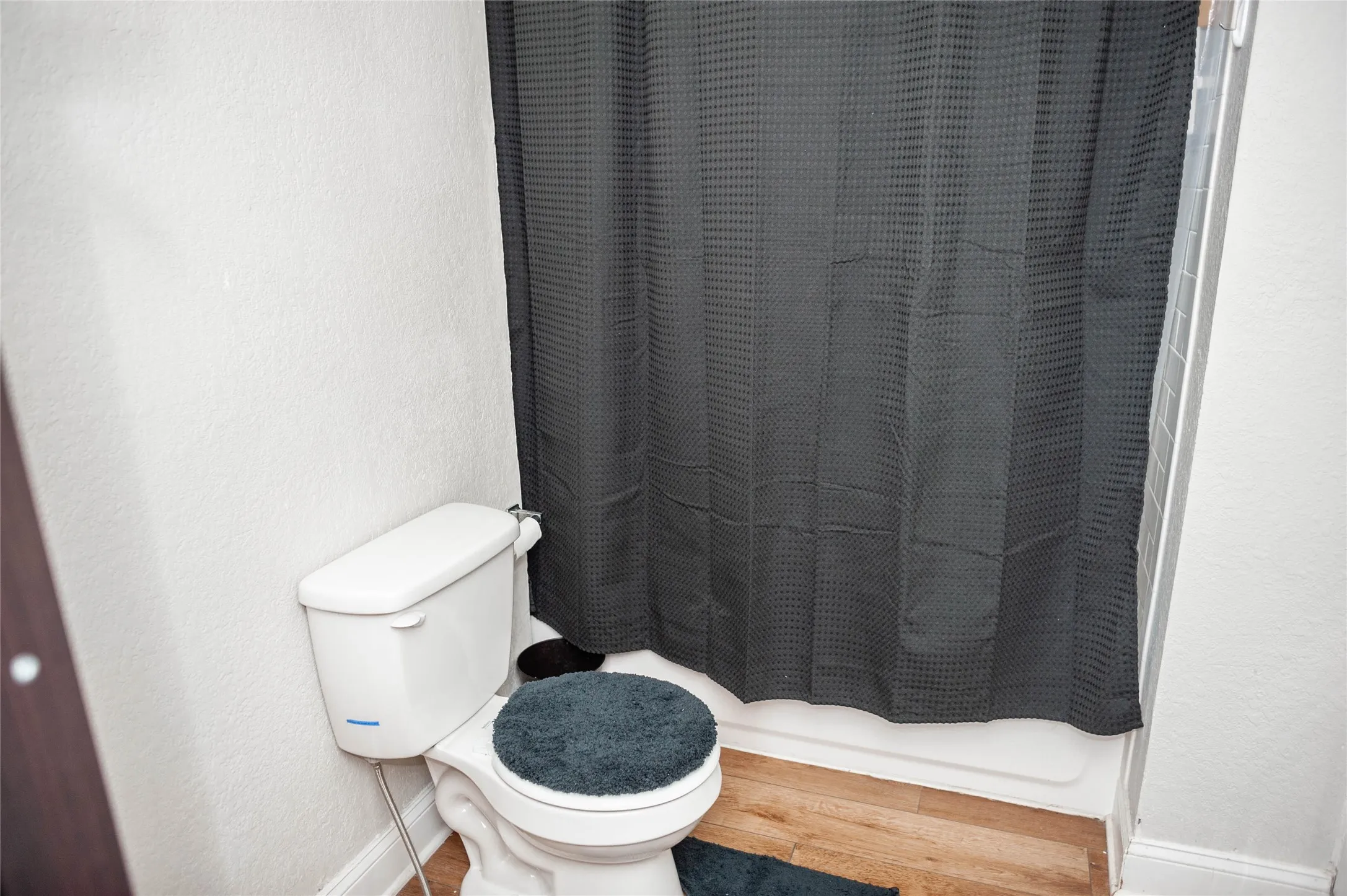 White toilet with a built-in shower enclosure and wood-finish flooring