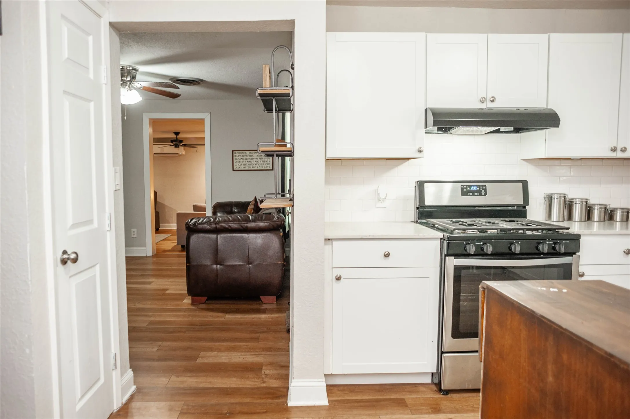 White shaker-style cabinetry, stainless steel range with overhead ventilation, light-toned countertops, and wood-finish flooring
