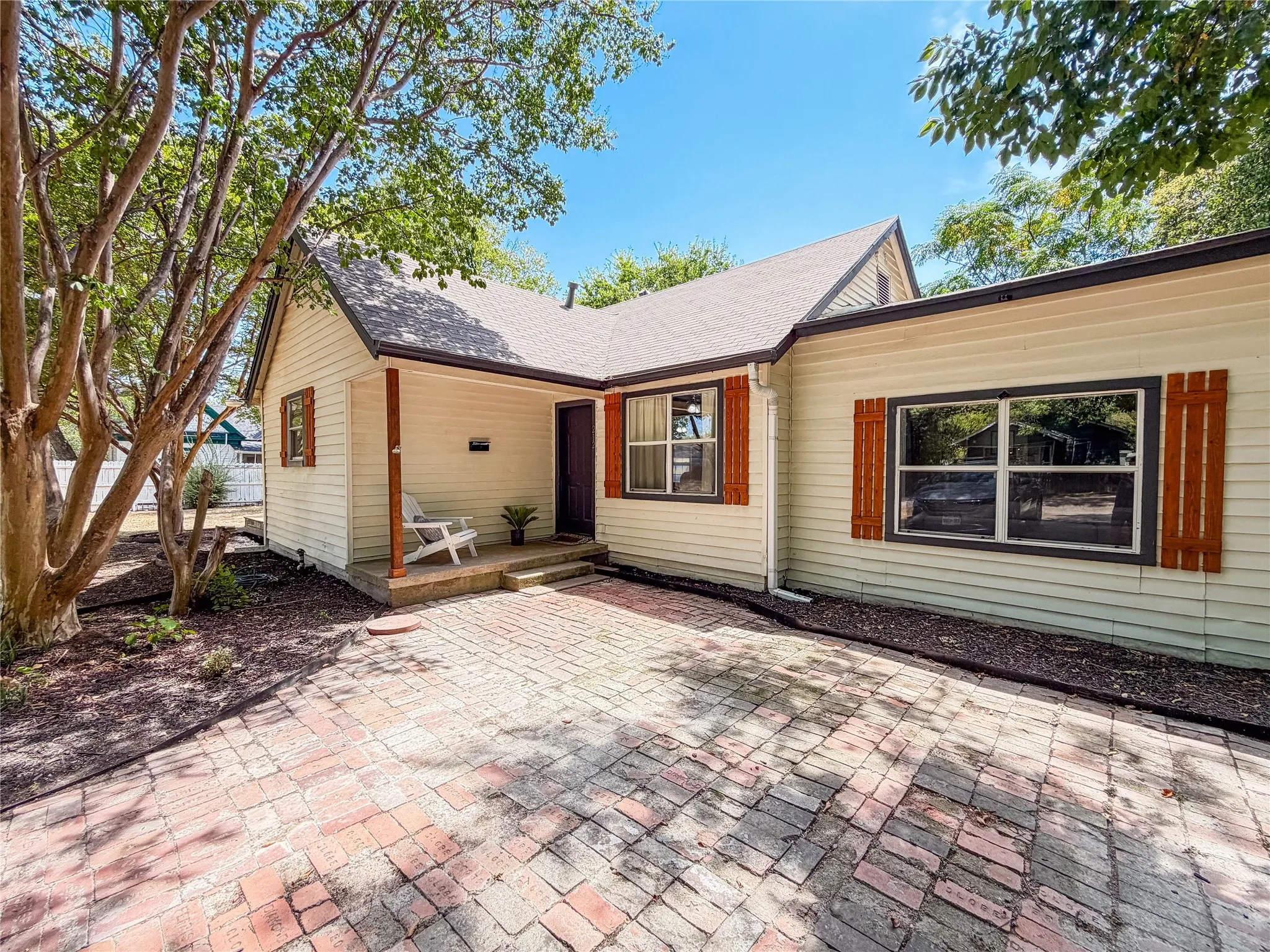 Siding exterior with a dark-pitched roof, wood-finish shutters, and a brick paver patio