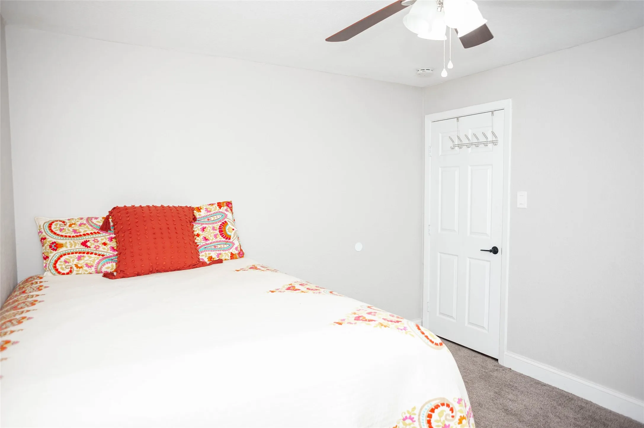 Neutral wall color, ceiling fan with light fixture, paneled door with dark hardware, and carpet flooring