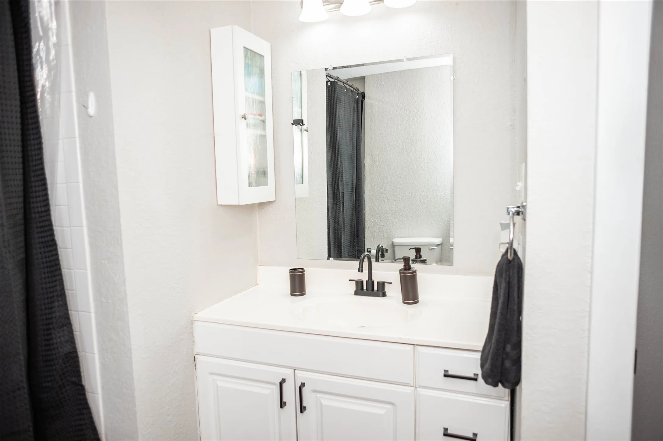 White vanity with cabinet storage and drawer space, white countertop, and dark-finish faucet