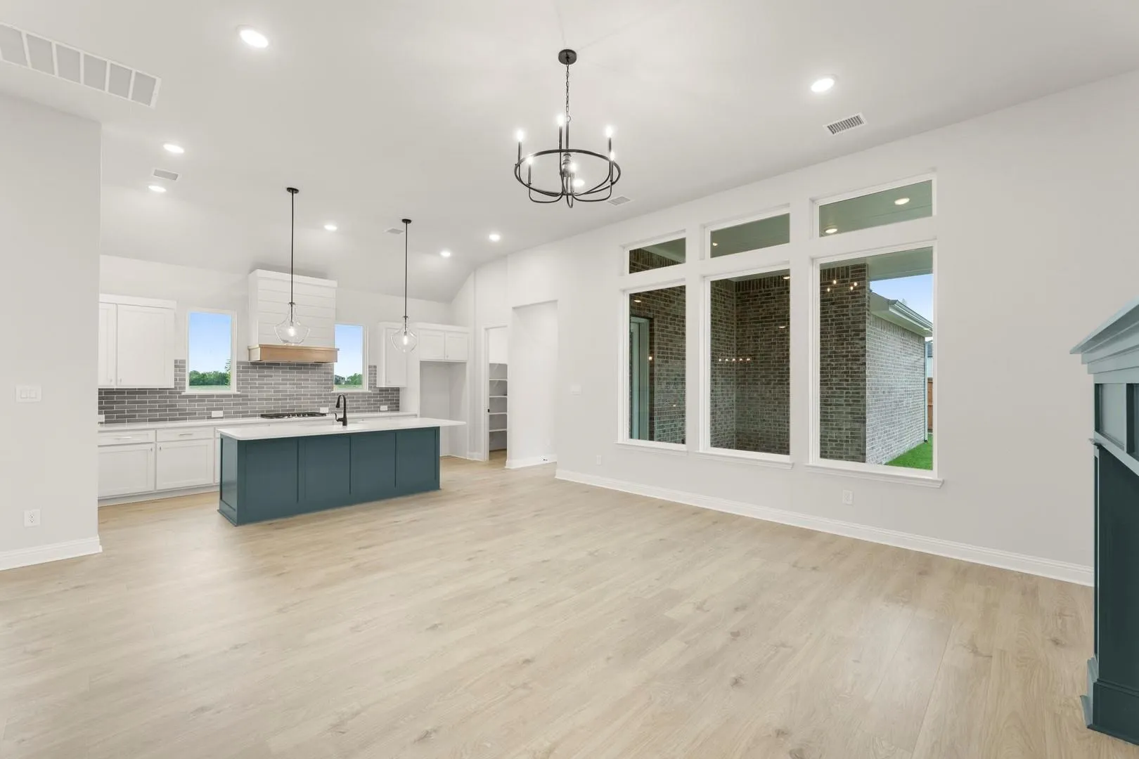 Spacious living area featuring light wood-finish flooring, a built-in fireplace with a teal mantel and tiled surround, and a contemporary chandelier