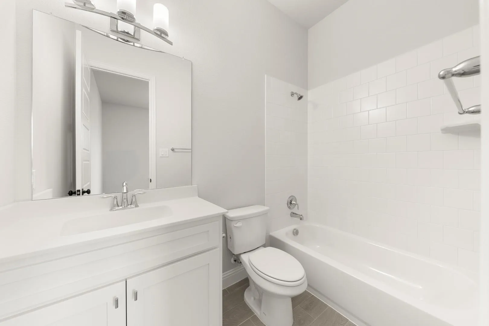 Clean and bright bathroom featuring a white vanity with dual sink setup, ample mirror with integrated lighting, ceramic tile surround, and an alcove bathtub with shower combination