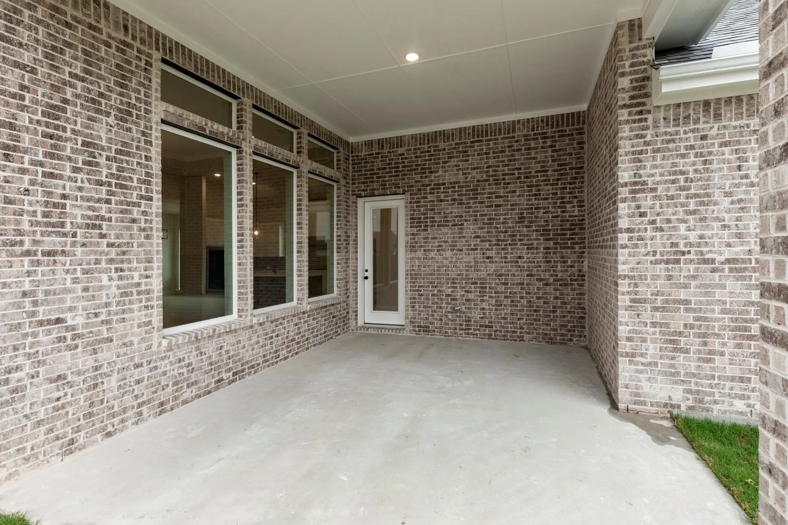 Covered patio featuring brick exterior walls, concrete flooring, and multiple glass doors and windows providing natural light and access to outdoor spaces