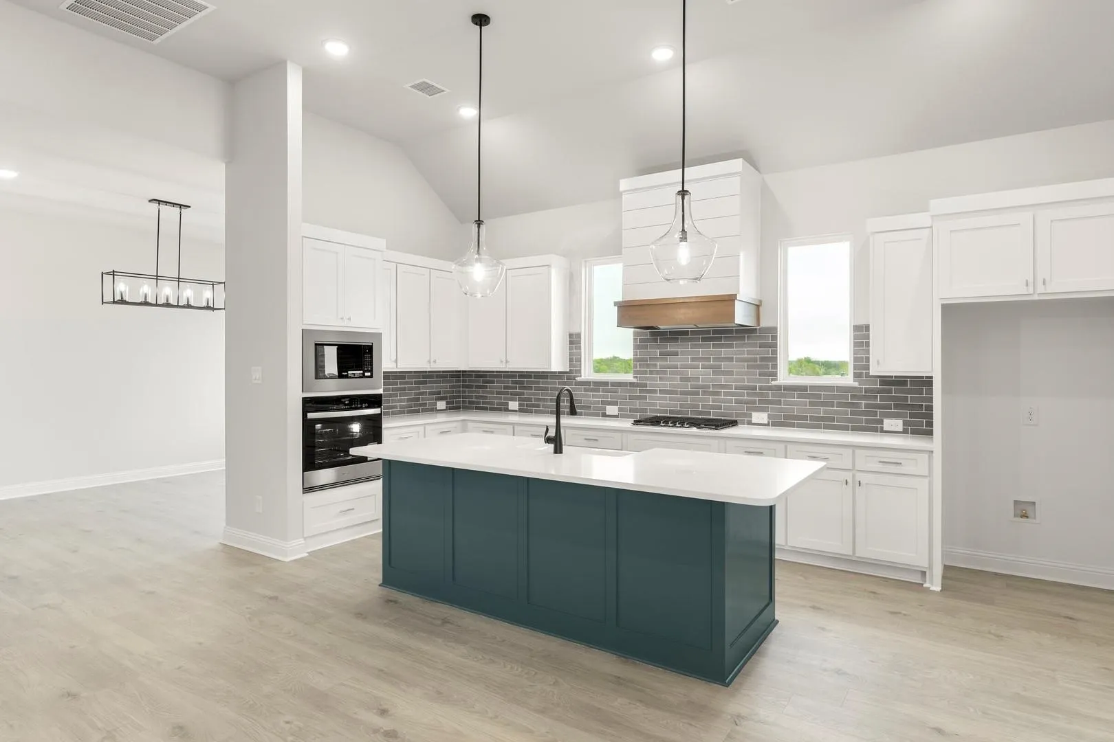 Modern kitchen featuring white shaker cabinetry, a teal-painted island with white quartz countertop, subway tile backsplash, stainless steel appliances, pendant lighting, wood-finish flooring, and abundant natural light from multiple windows