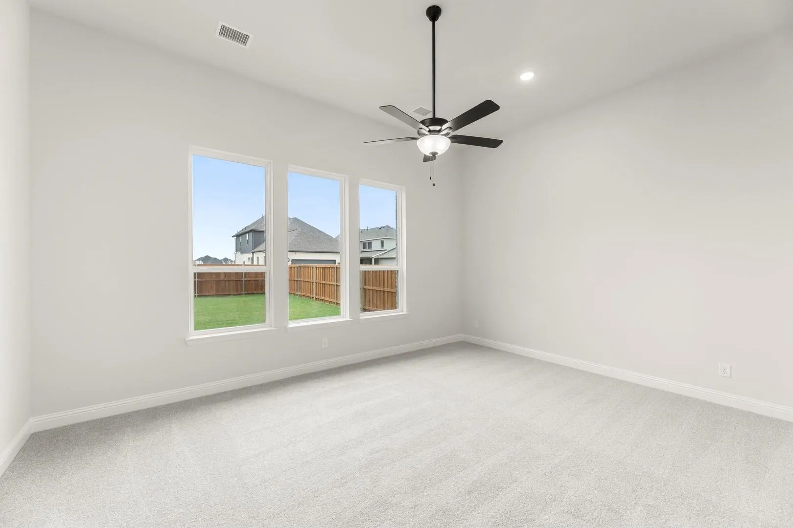 Bright secondary bedroom featuring expansive triple-panel glass doors with clear sightlines to the exterior, light neutral carpet flooring, ceiling-mounted fan with integrated lighting fixture, and fresh white walls throughout