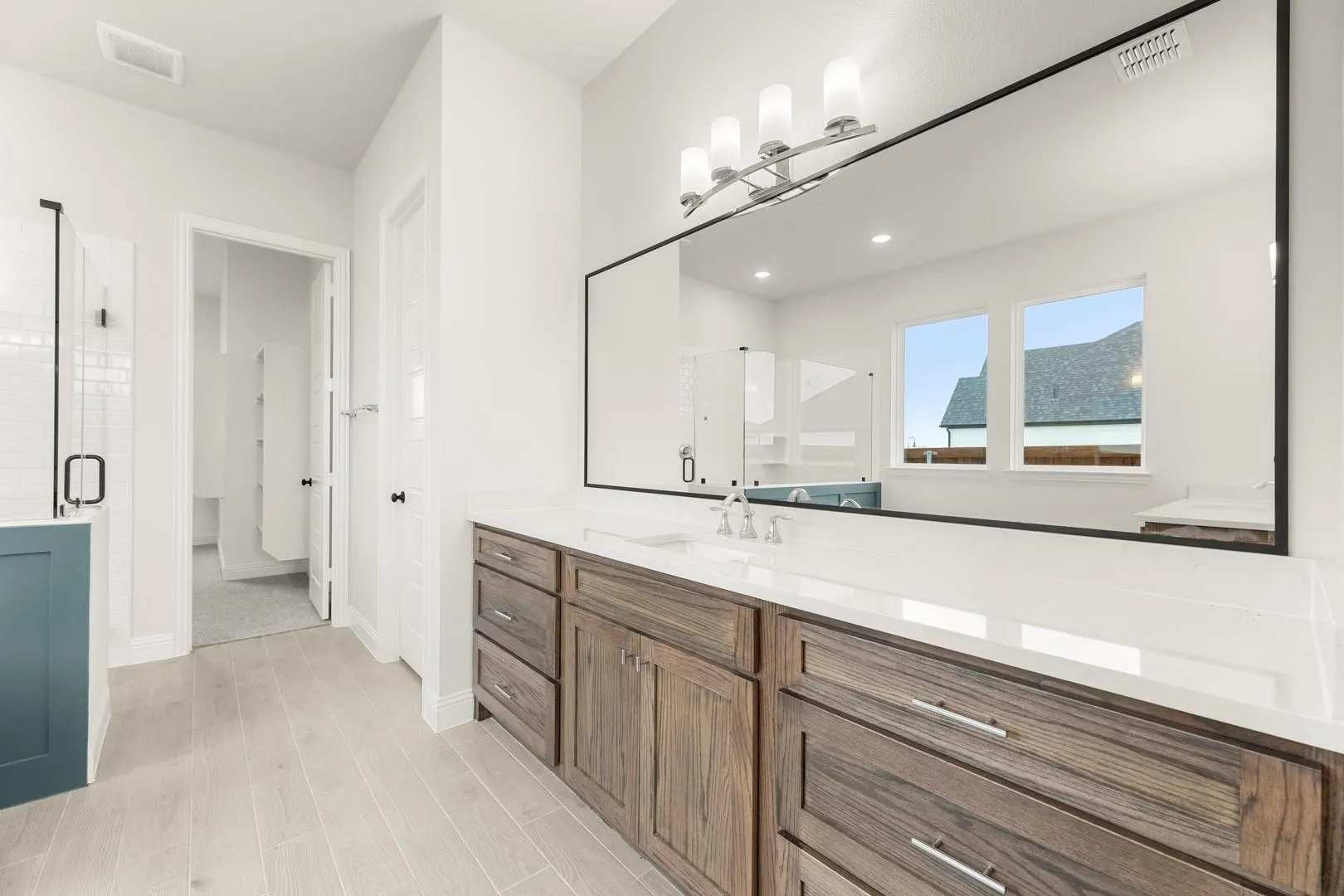 Spa-inspired primary bathroom featuring a wood-finish vanity with multiple drawers, white quartz countertop, and an expansive framed mirror with integrated lighting