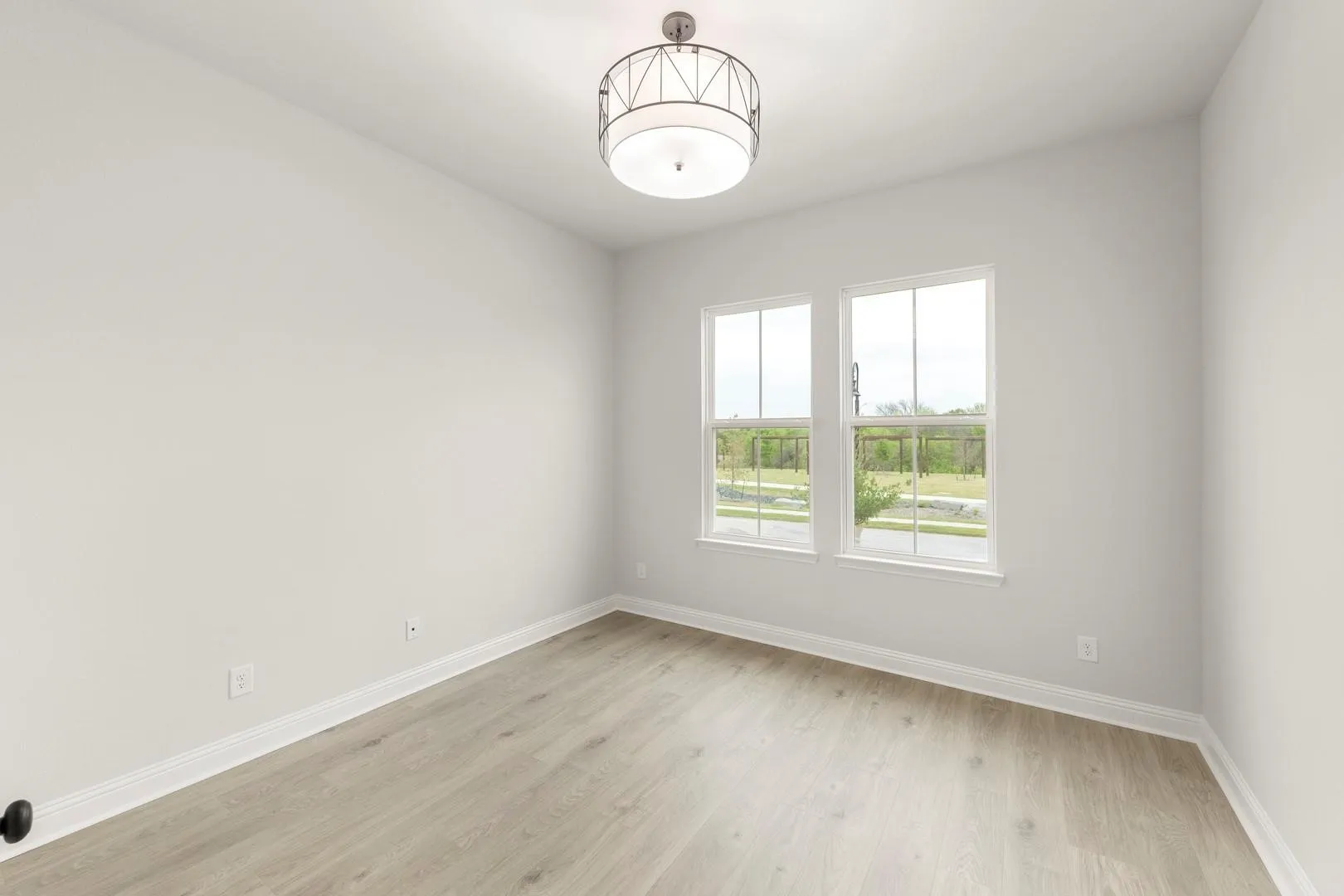 Bright secondary bedroom featuring expansive double windows with natural light, light wood-finish flooring, crisp white walls, and a ceiling-mounted fixture