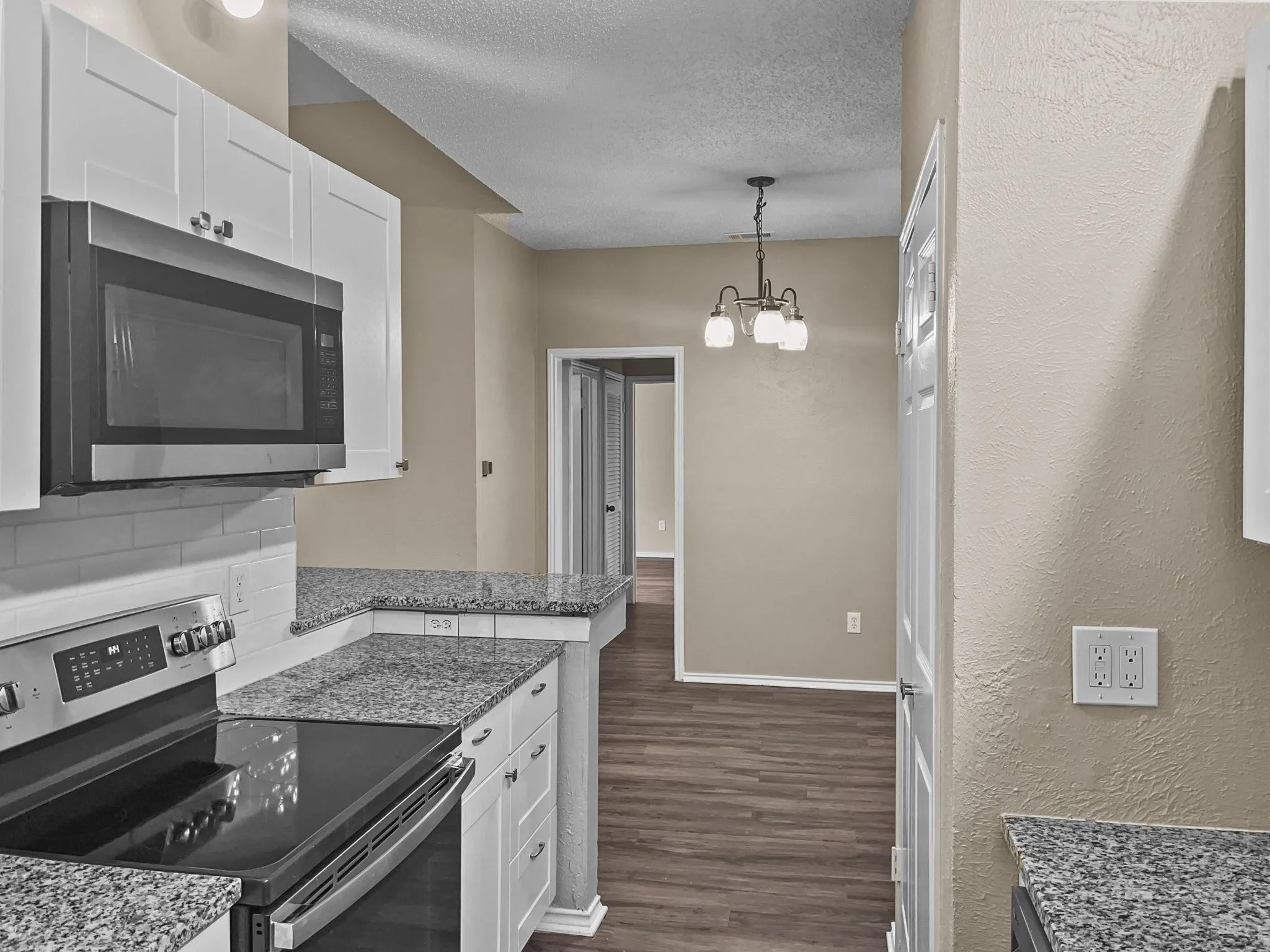 Kitchen featuring white cabinetry, granite countertops, stainless steel appliances, a white subway tile backsplash, and wood-finish flooring