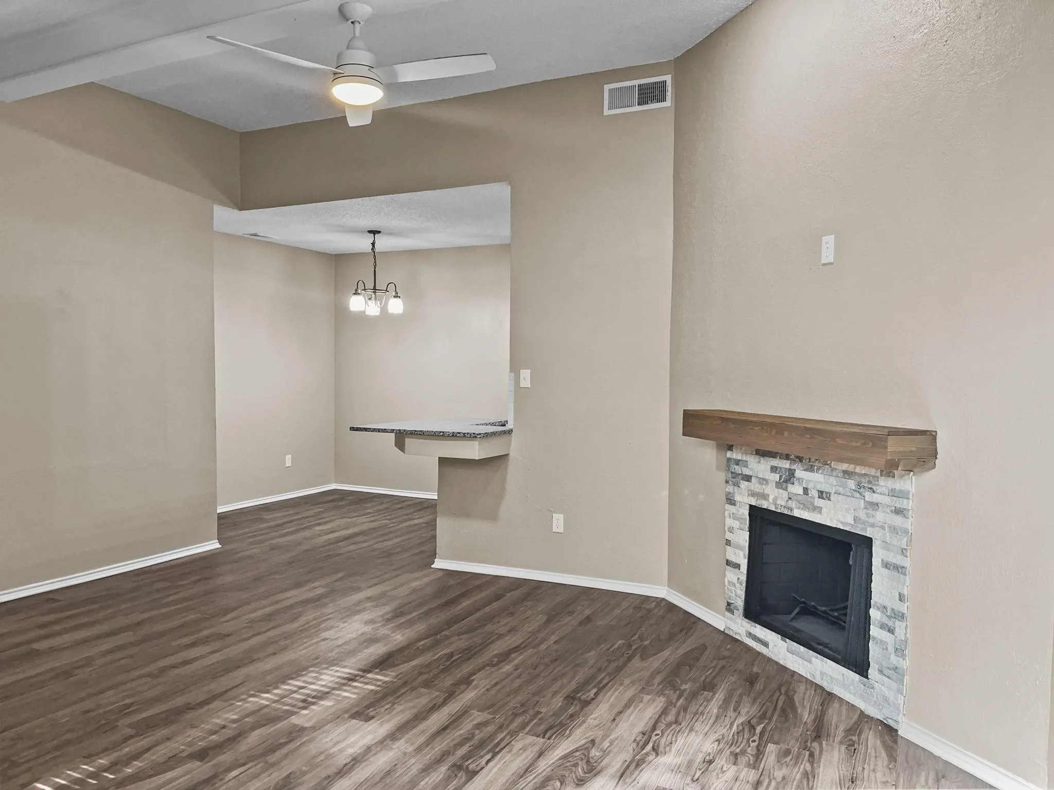 Living area featuring wood-finish flooring, a contemporary ceiling fan, and a fireplace with a stone surround and wood mantel