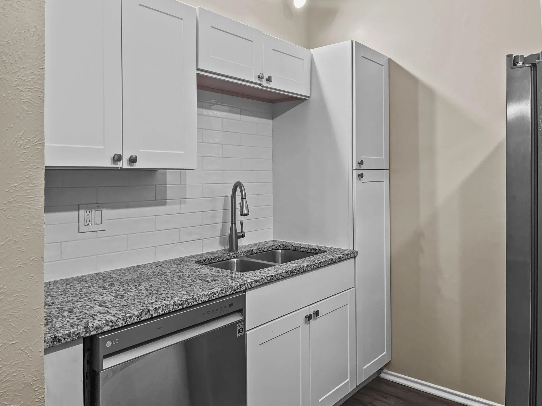 Kitchenette featuring granite-finish countertops, subway tile backsplash, stainless steel dishwasher, and a dual-basin sink with a modern faucet