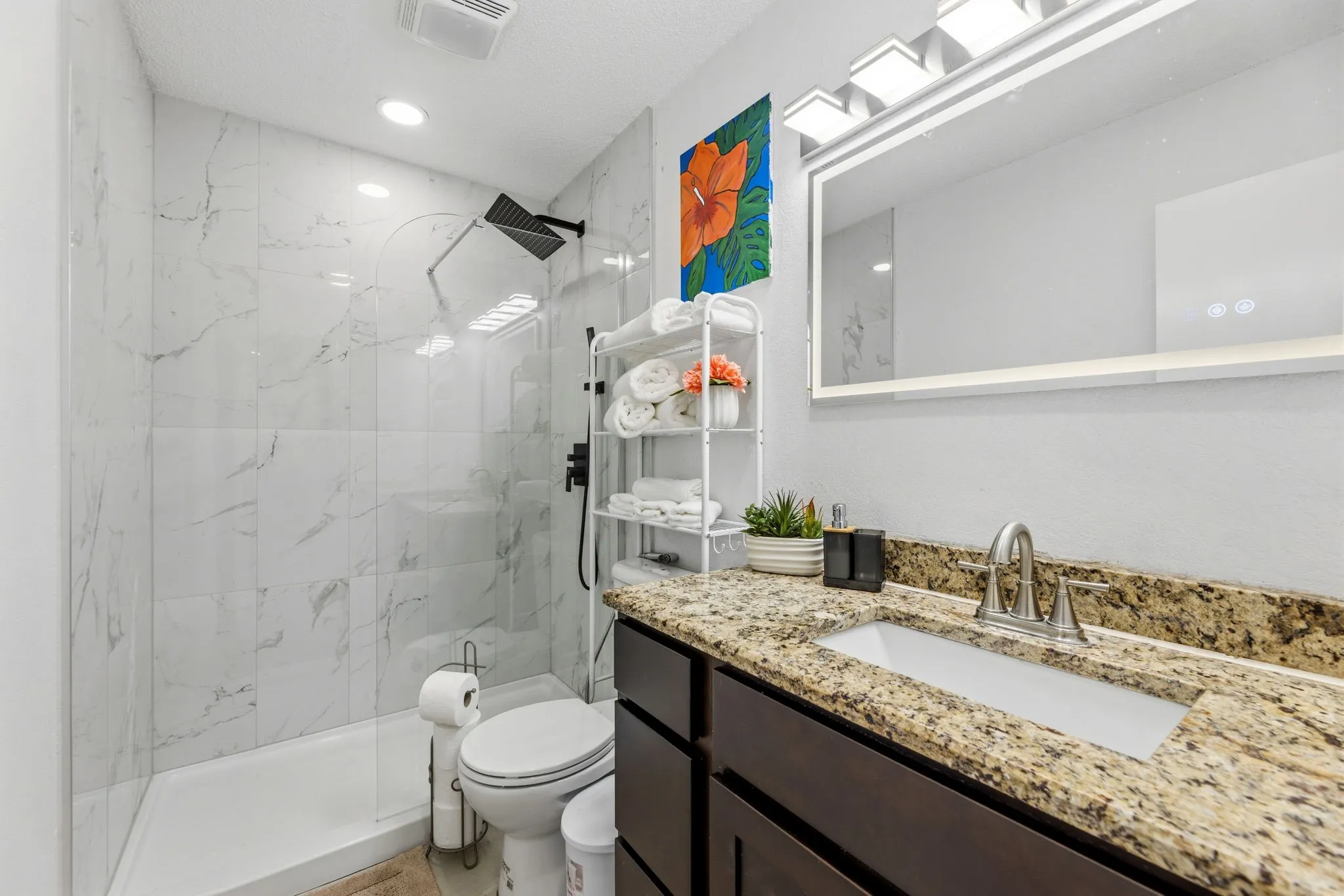 Bathroom featuring a dark wood-finish vanity with a light-colored granite countertop, an undermount sink, and a framed mirror with integrated lighting