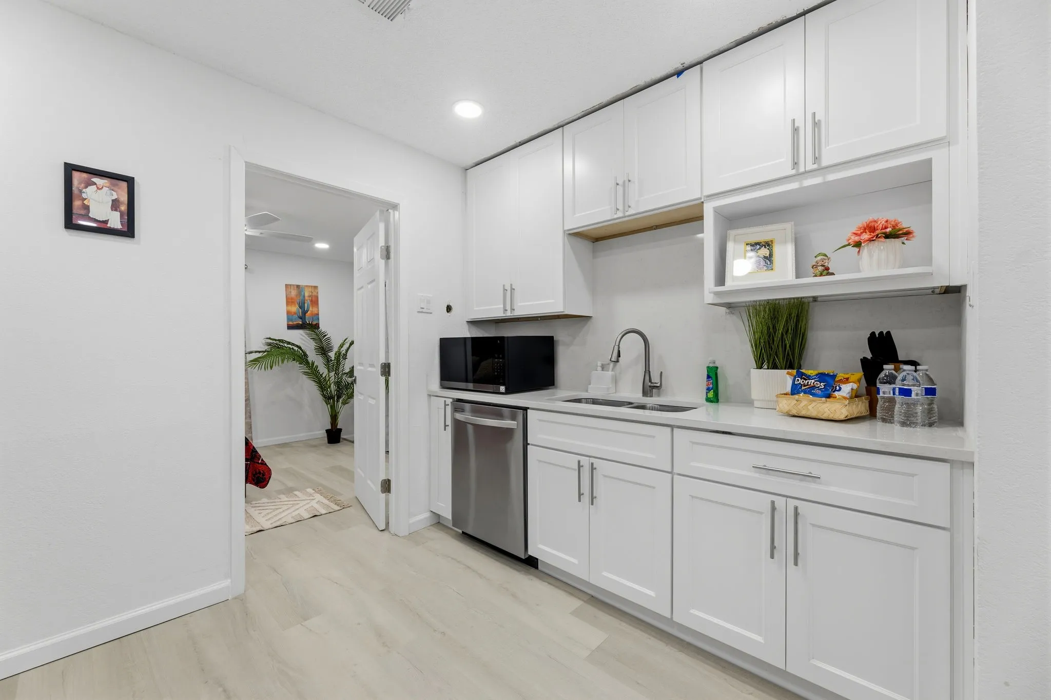 Contemporary kitchen featuring white shaker cabinetry, light-toned countertops, a stainless steel sink with a gooseneck faucet, a built-in dishwasher, and wood-finish flooring