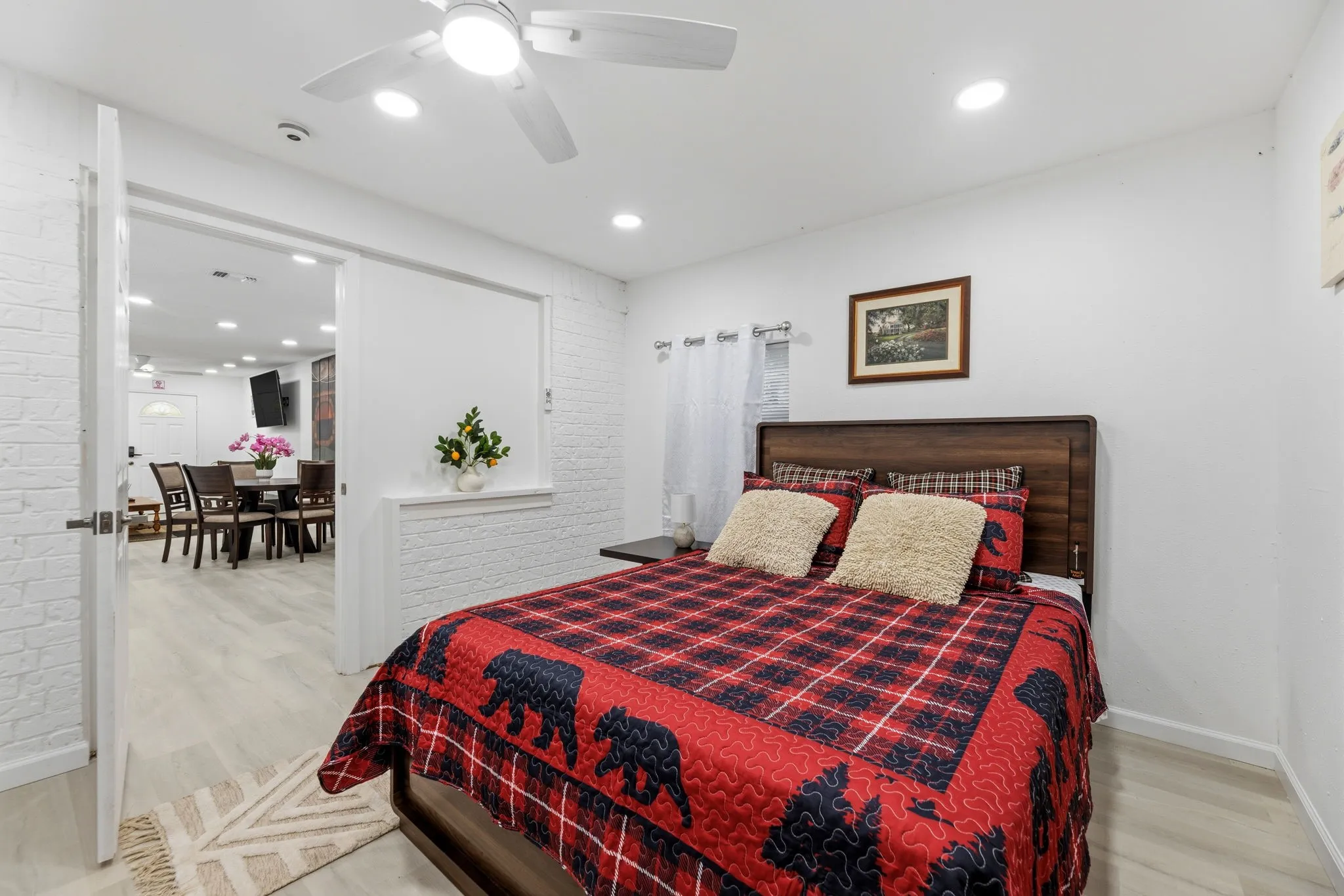 Comfortable bedroom showcasing a wood-finish plank flooring, ceiling fan with integrated lighting, and a wood-frame bed with upholstered headboard