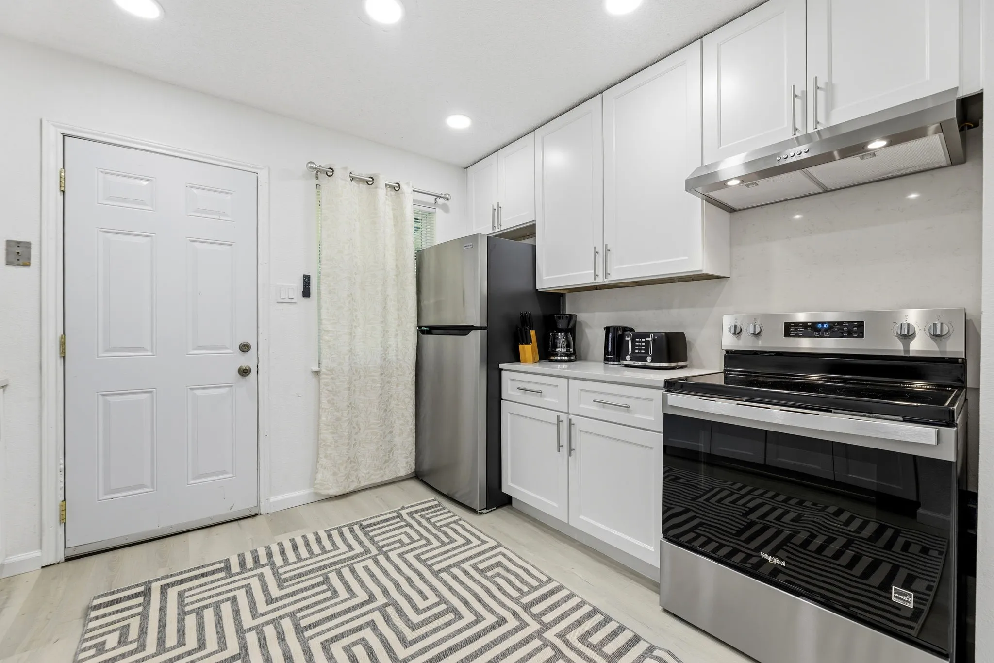Modern kitchen featuring white shaker cabinetry, stainless steel range with overhead ventilation, and light-toned wood-finish flooring