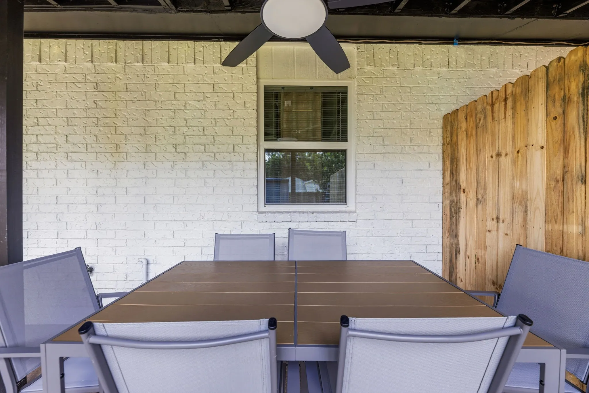 Covered patio featuring a white painted brick wall, a window with blinds, and a wood privacy fence