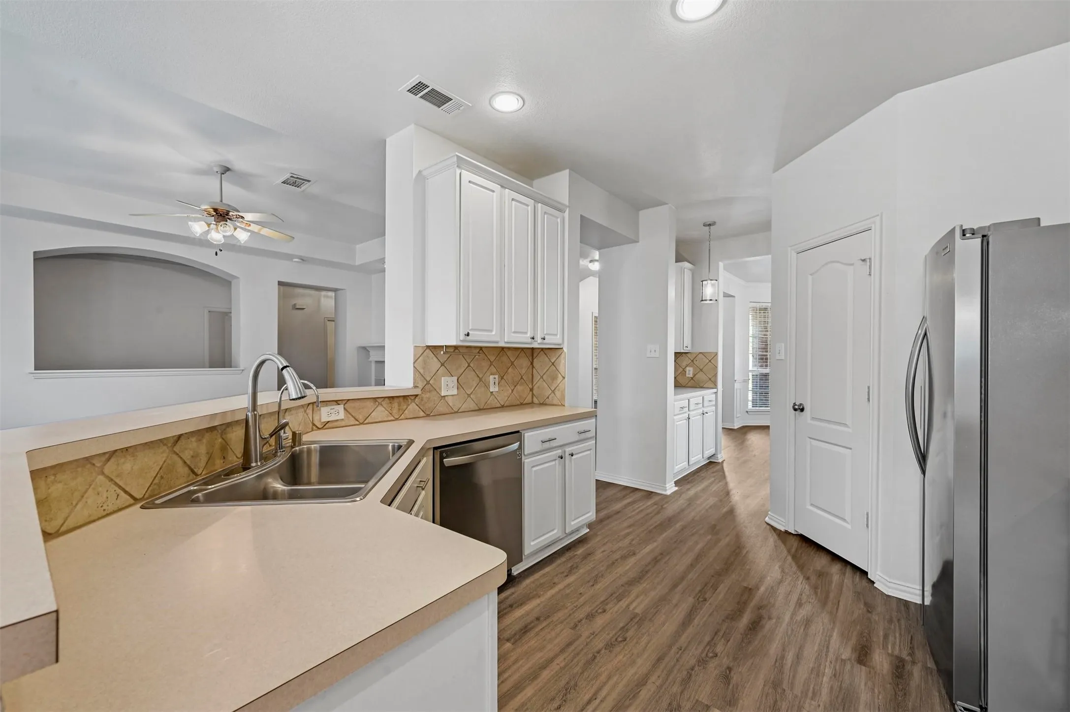 Spacious kitchen featuring an undermount double-basin sink, stainless steel dishwasher, white cabinetry, neutral countertops, and wood-finish flooring