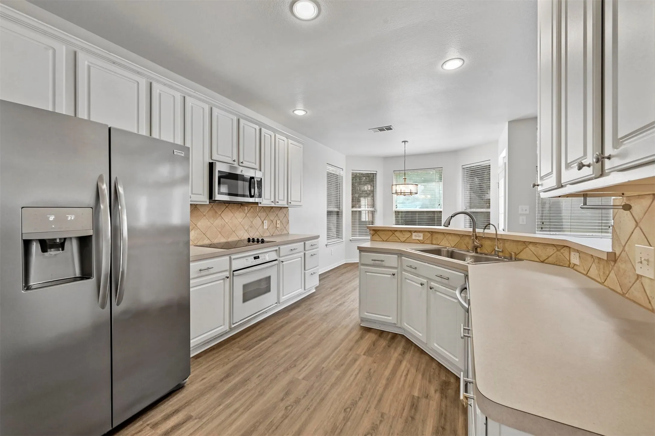 Kitchen featuring wood-finish flooring, white cabinetry, stainless steel appliances, and a tiled backsplash