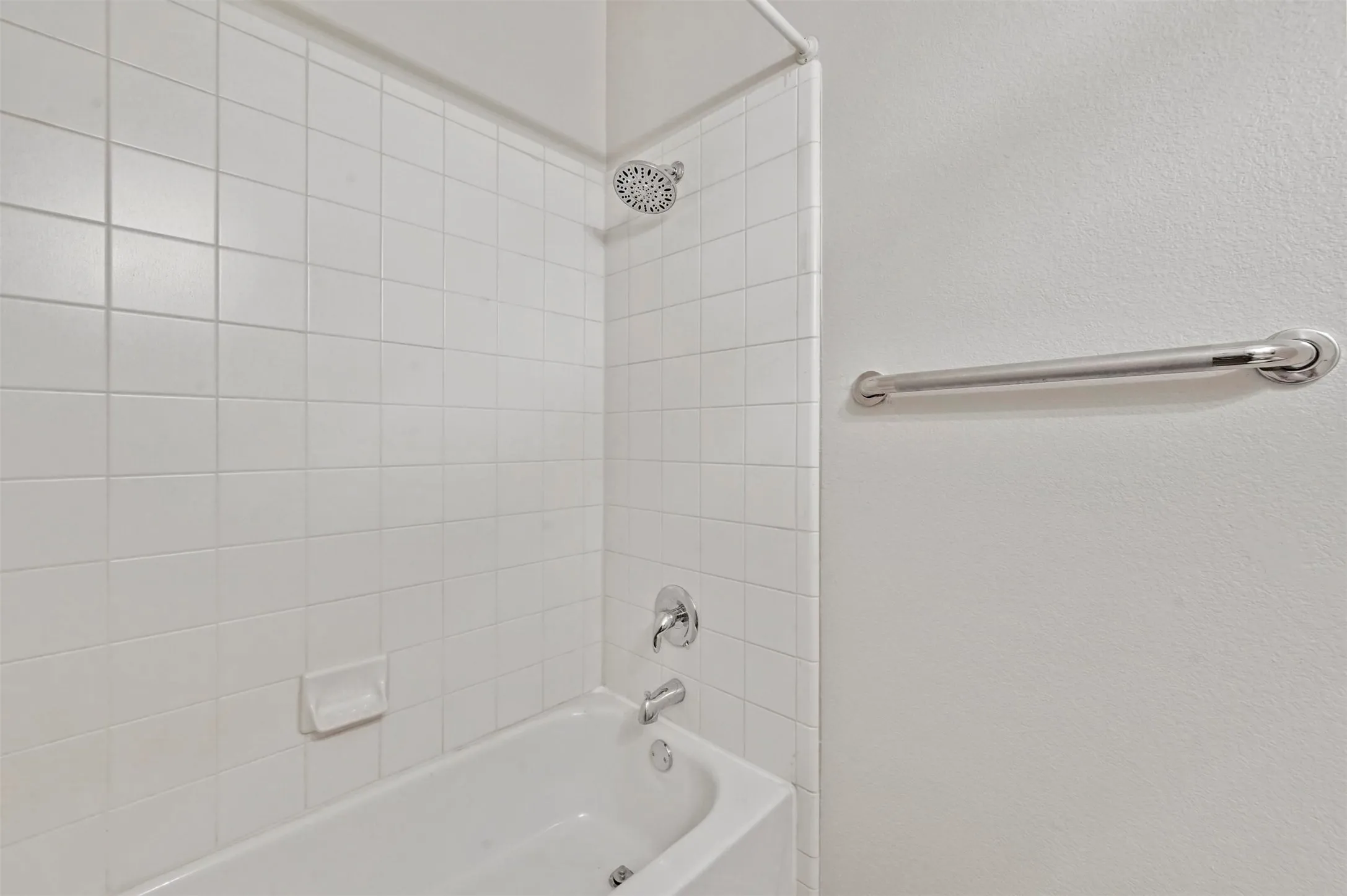 Shower and tub combination featuring white square tiling, chrome fixtures, and a wall-mounted grab bar
