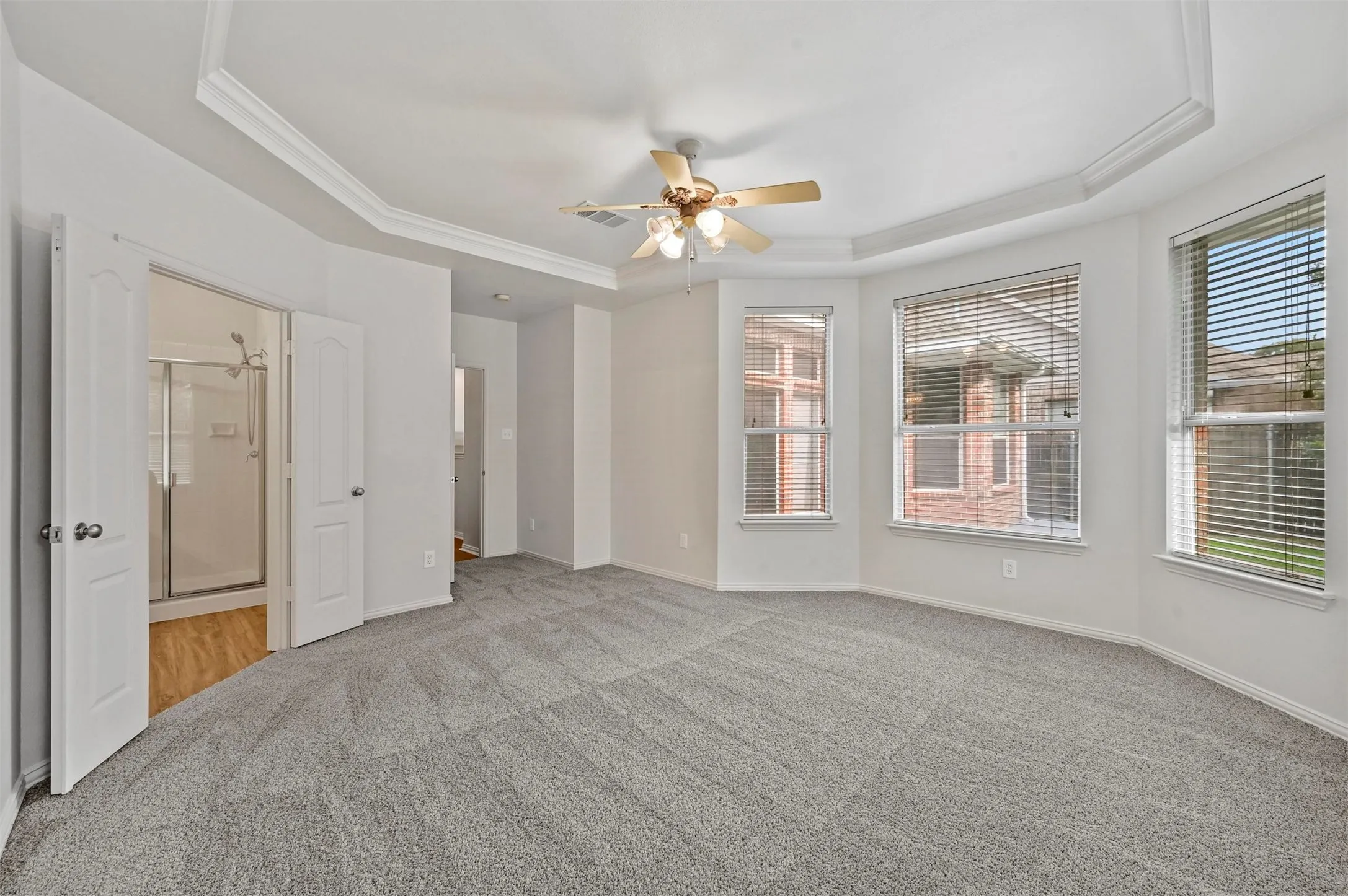 Spacious room featuring gray carpeting, a tray ceiling with crown molding, and a ceiling fan