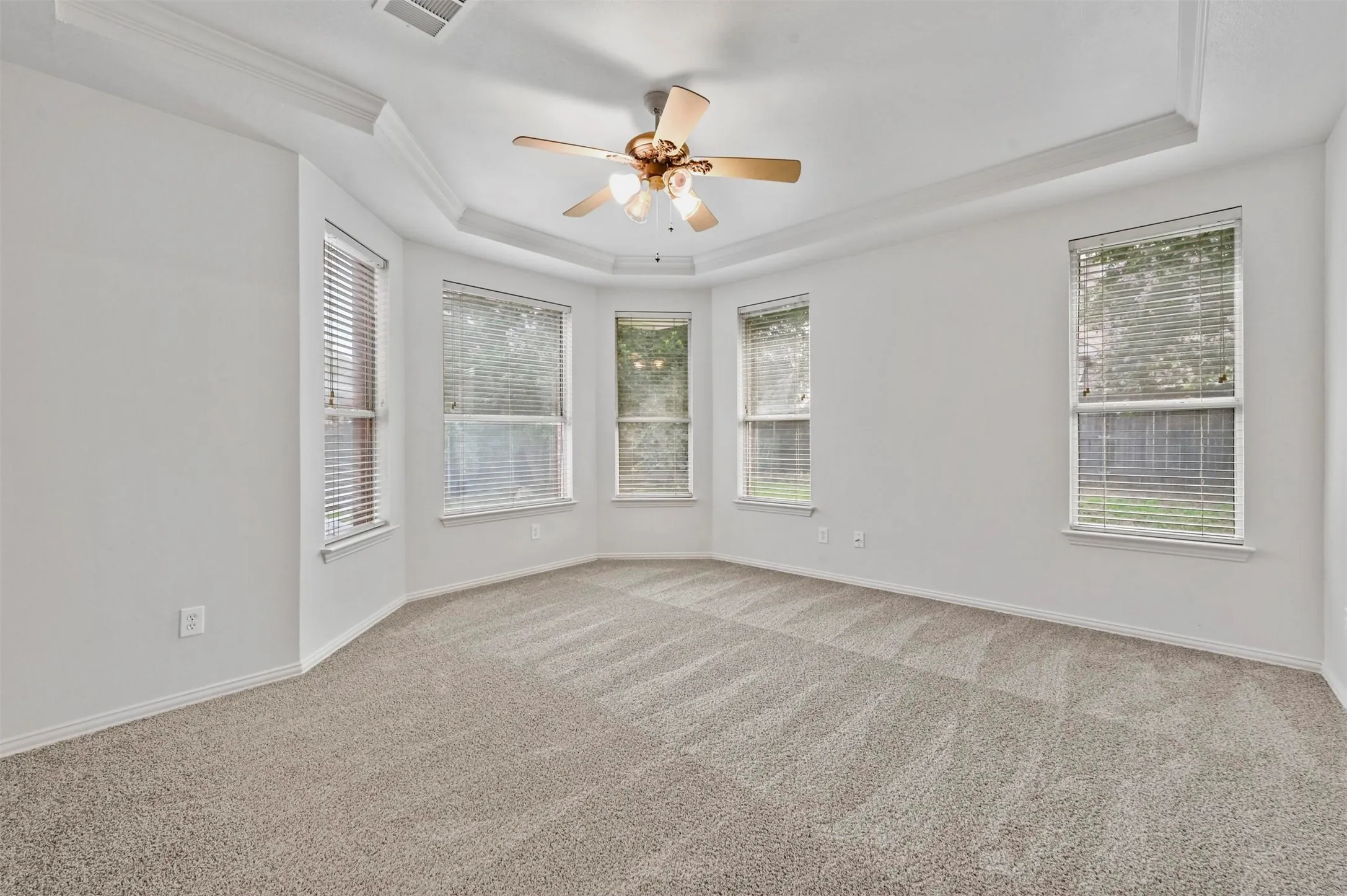 Spacious room featuring light-toned carpet flooring and a tray ceiling with a built-in ceiling fan