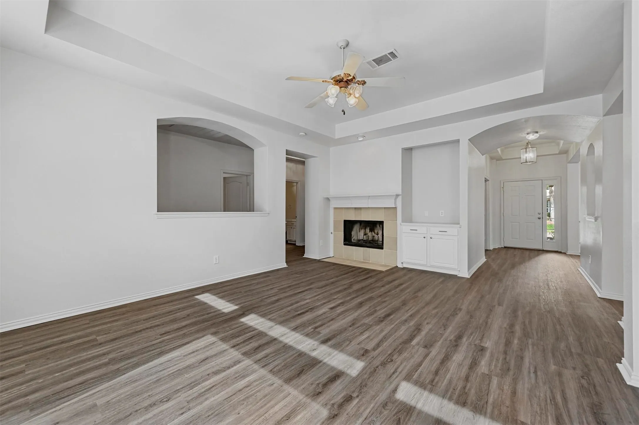 Expansive living area featuring wood-finish flooring, a tray ceiling, and a fireplace with a tile surround and mantle