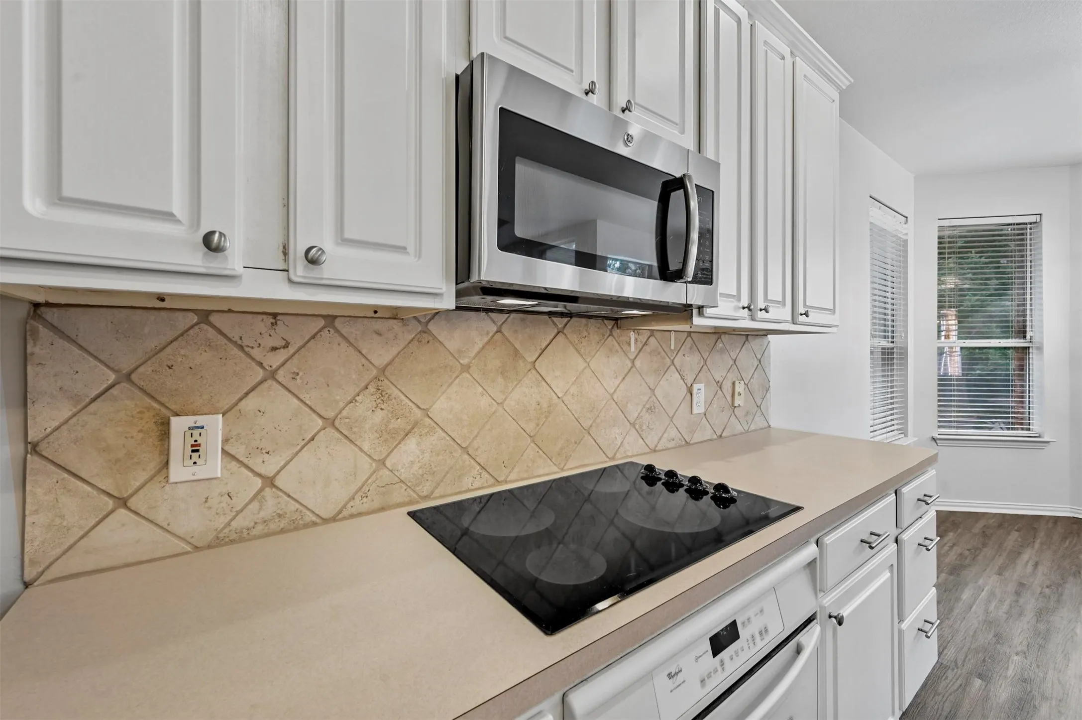 Kitchen featuring white cabinetry with brushed nickel hardware, stainless steel over-the-range microwave, built-in cooktop, and tile backsplash