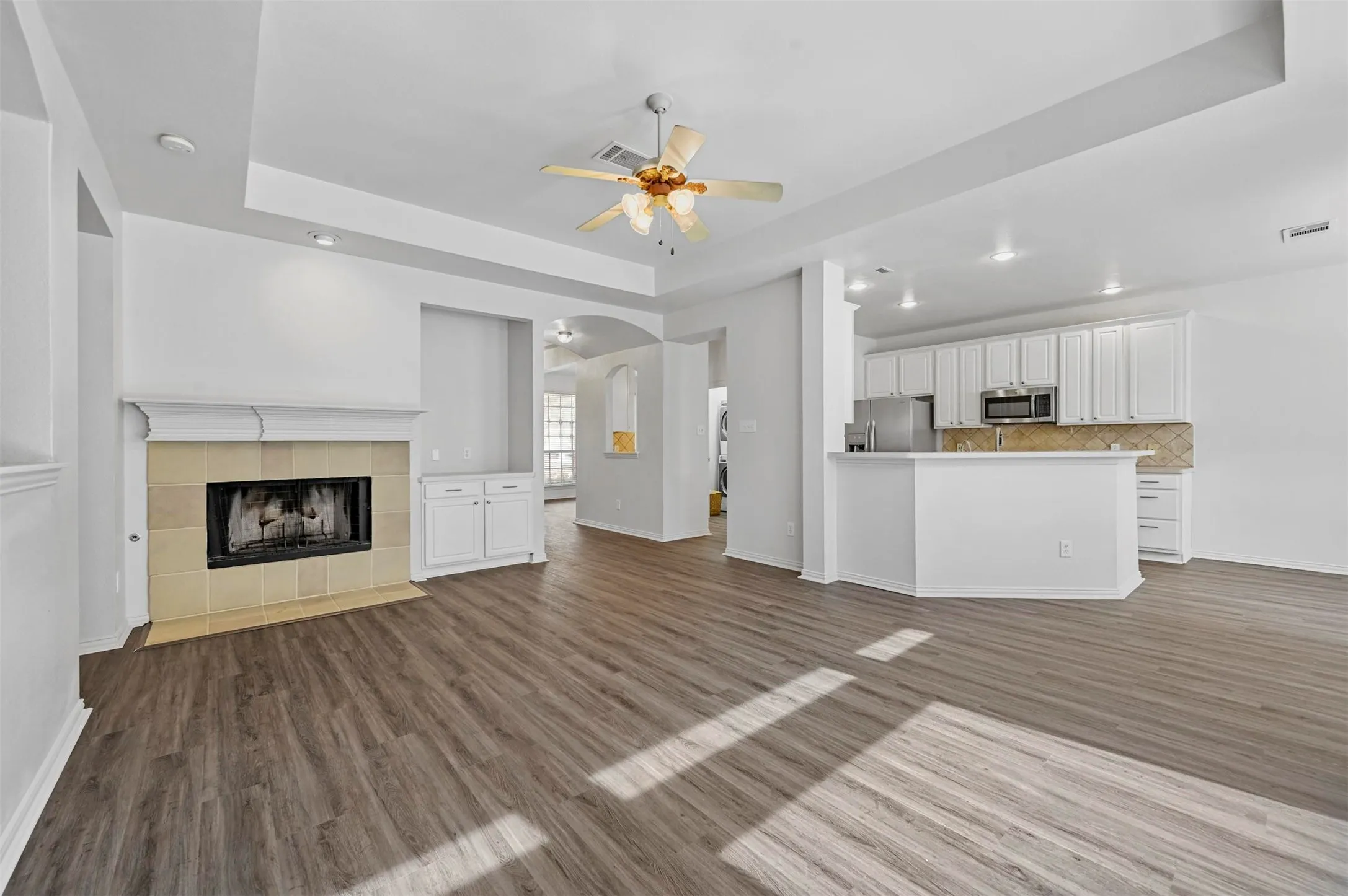 Open-concept living space featuring wood-finish flooring, a fireplace with a stone surround and mantel, built-in cabinetry, recessed lighting, and a ceiling fan