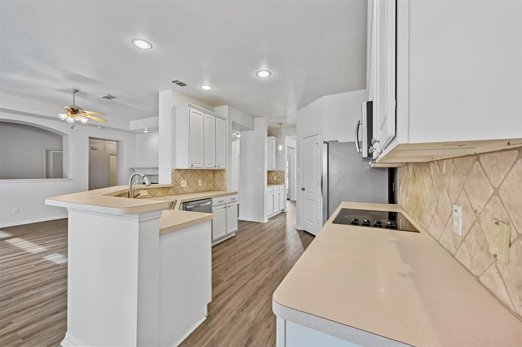 Kitchen featuring white cabinetry, light-toned countertops, a diagonal tile backsplash, and wood-finish flooring
