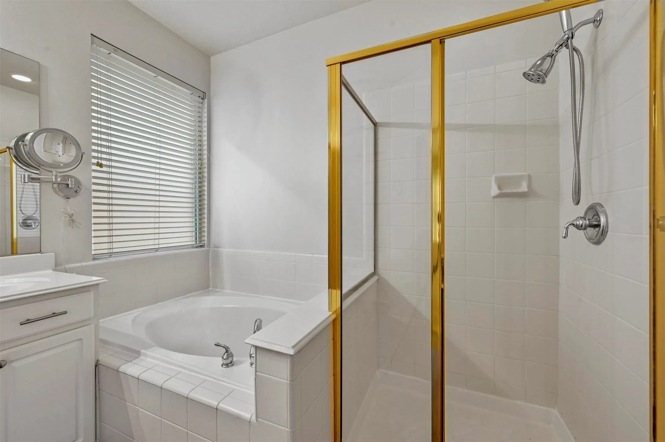 Bathroom featuring a built-in tub, tiled shower with gold-toned frame, and a vanity with a white countertop