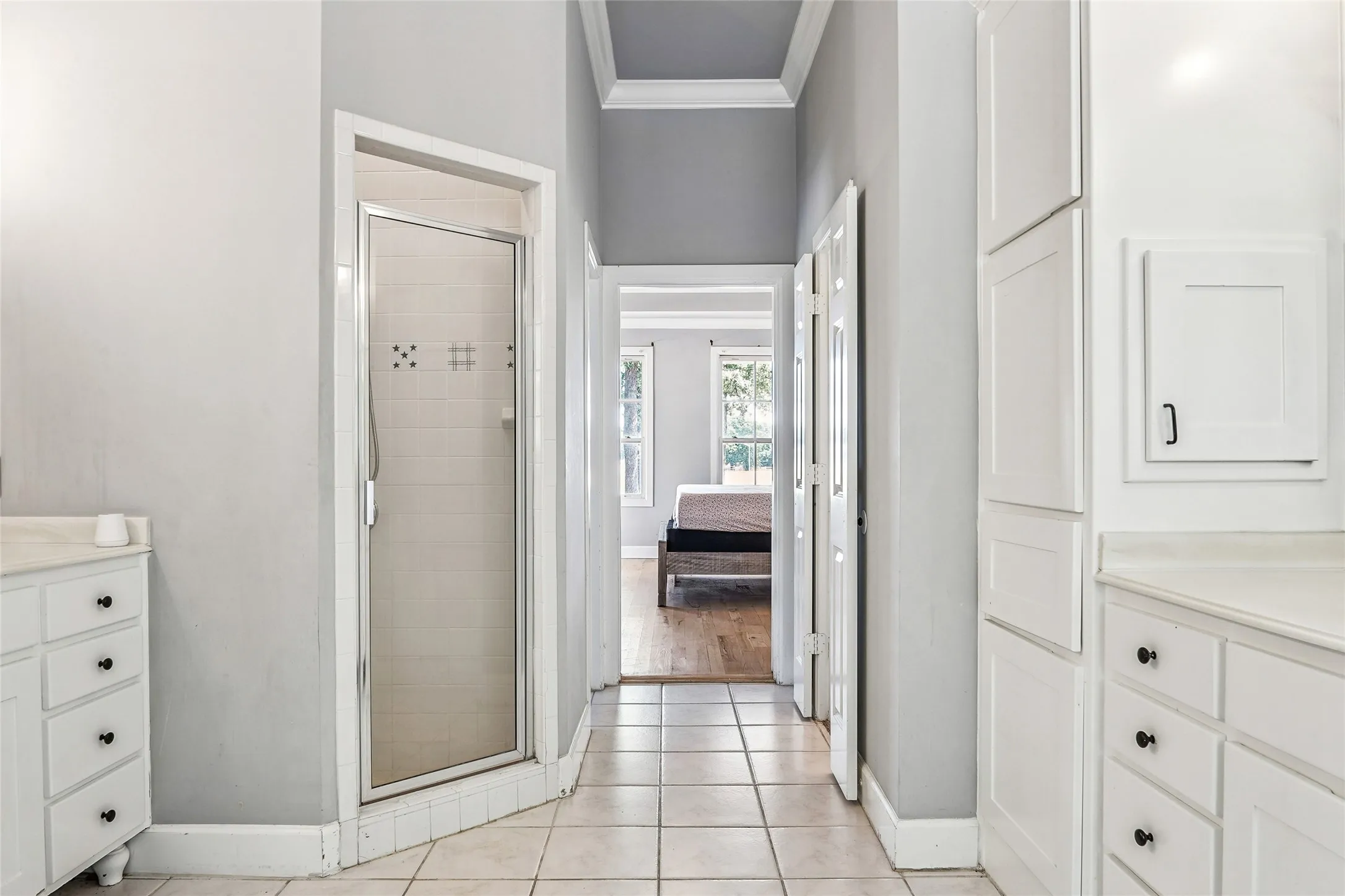 Shower enclosure with tiled walls and glass door, complemented by white cabinetry, light countertops, and square floor tiles
