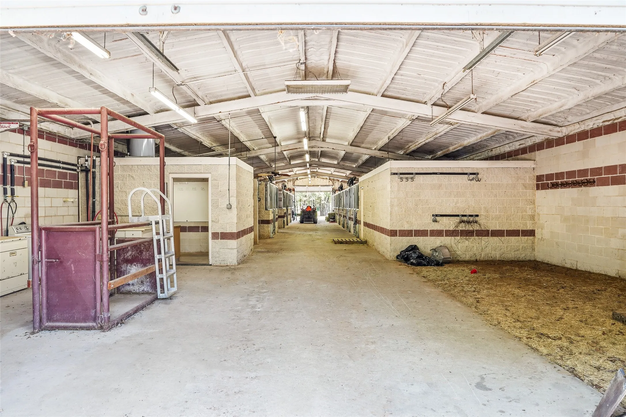 Covered barn structure featuring concrete flooring, exposed beam ceiling, and fluorescent lighting
