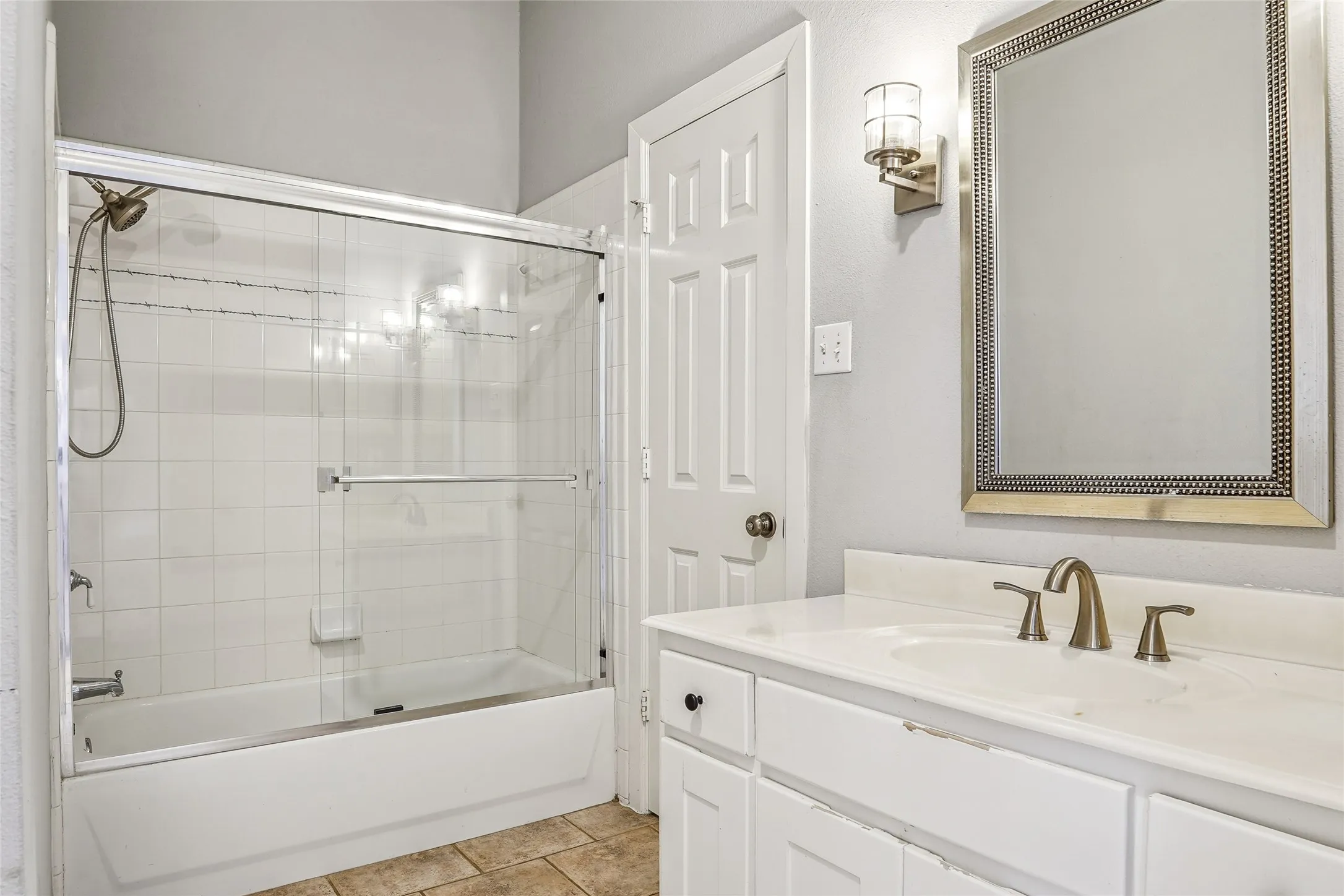 Bathroom featuring a vanity with an integrated sink, a framed mirror, and a tub with a glass shower enclosure