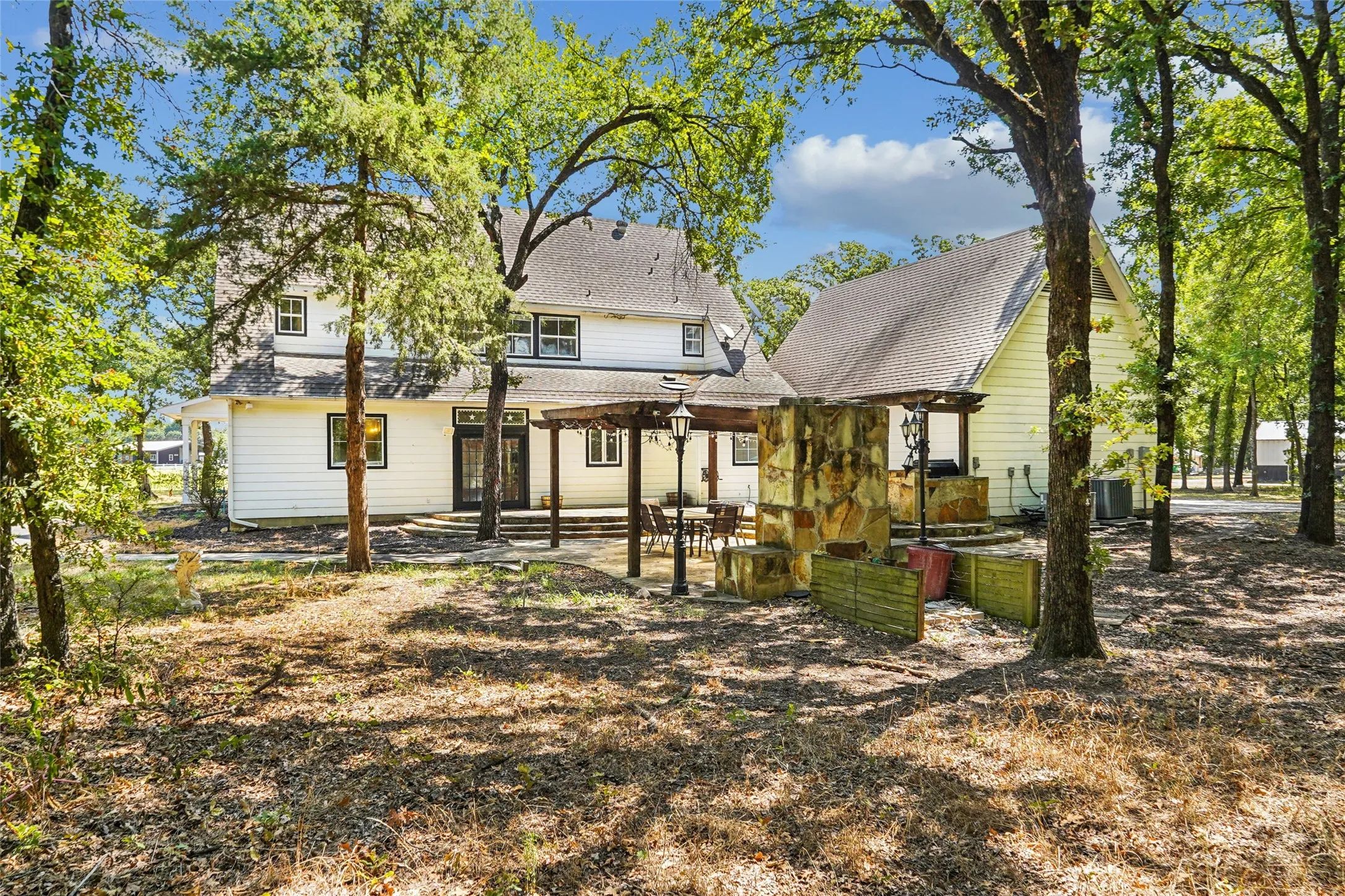 Expansive backyard featuring a stone patio, a wood pergola, and mature trees providing natural shade