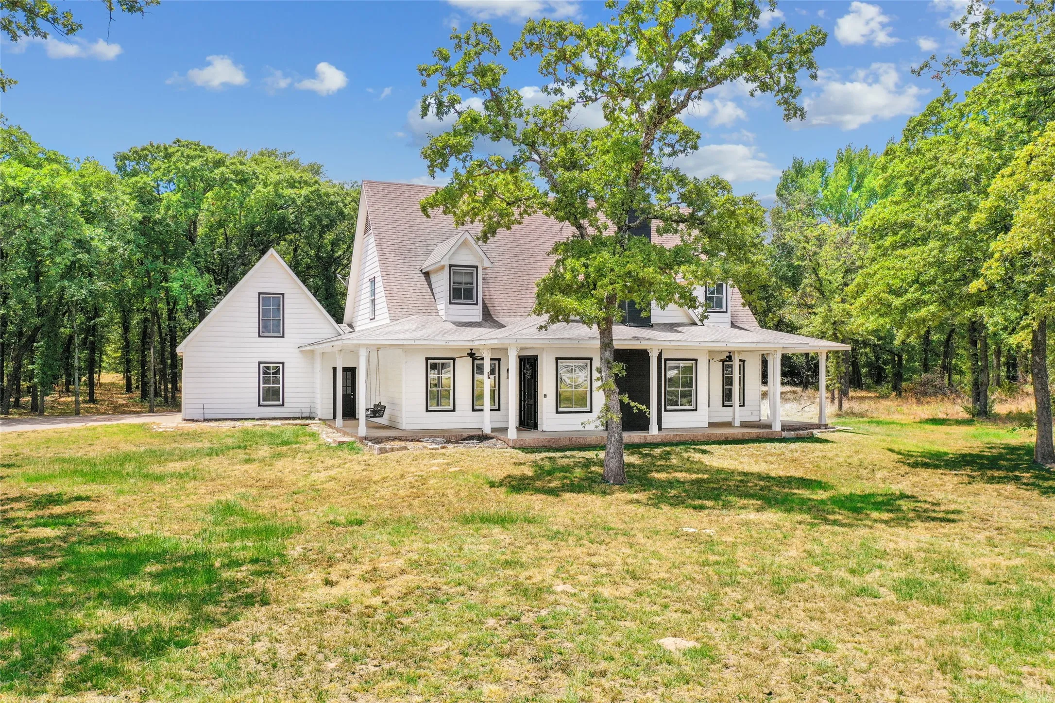 White farmhouse-style residence featuring a wide front porch with white columns, dormer windows, and a black front door
