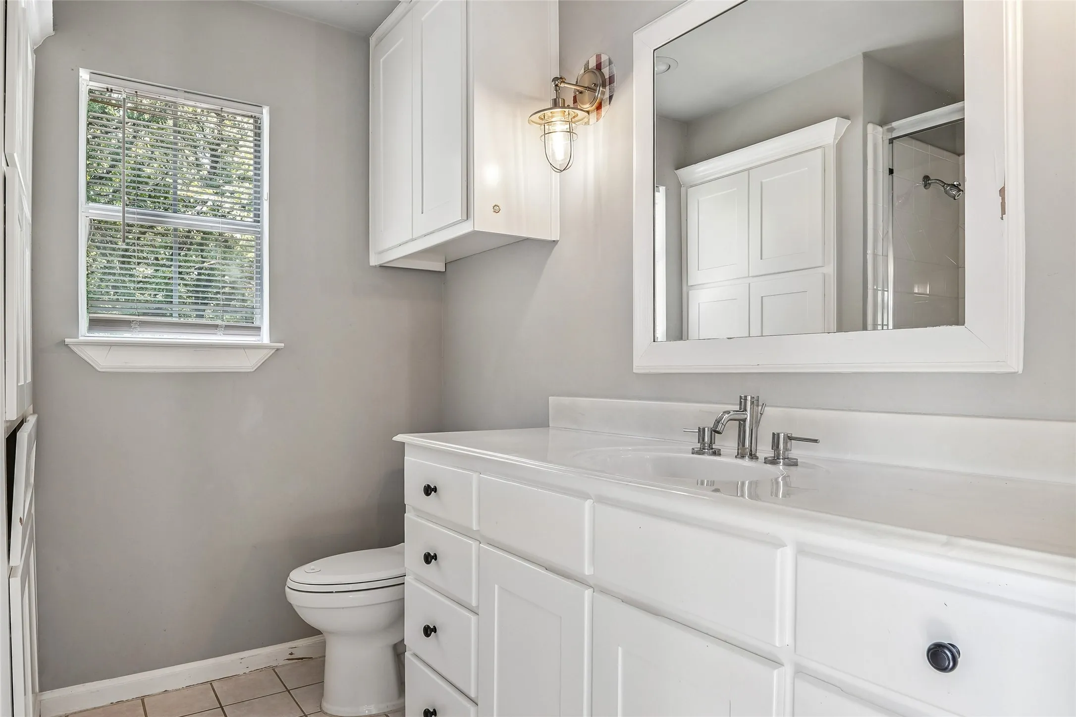 Bathroom featuring a white vanity with integrated sink, white shaker-style cabinetry, and a framed mirror