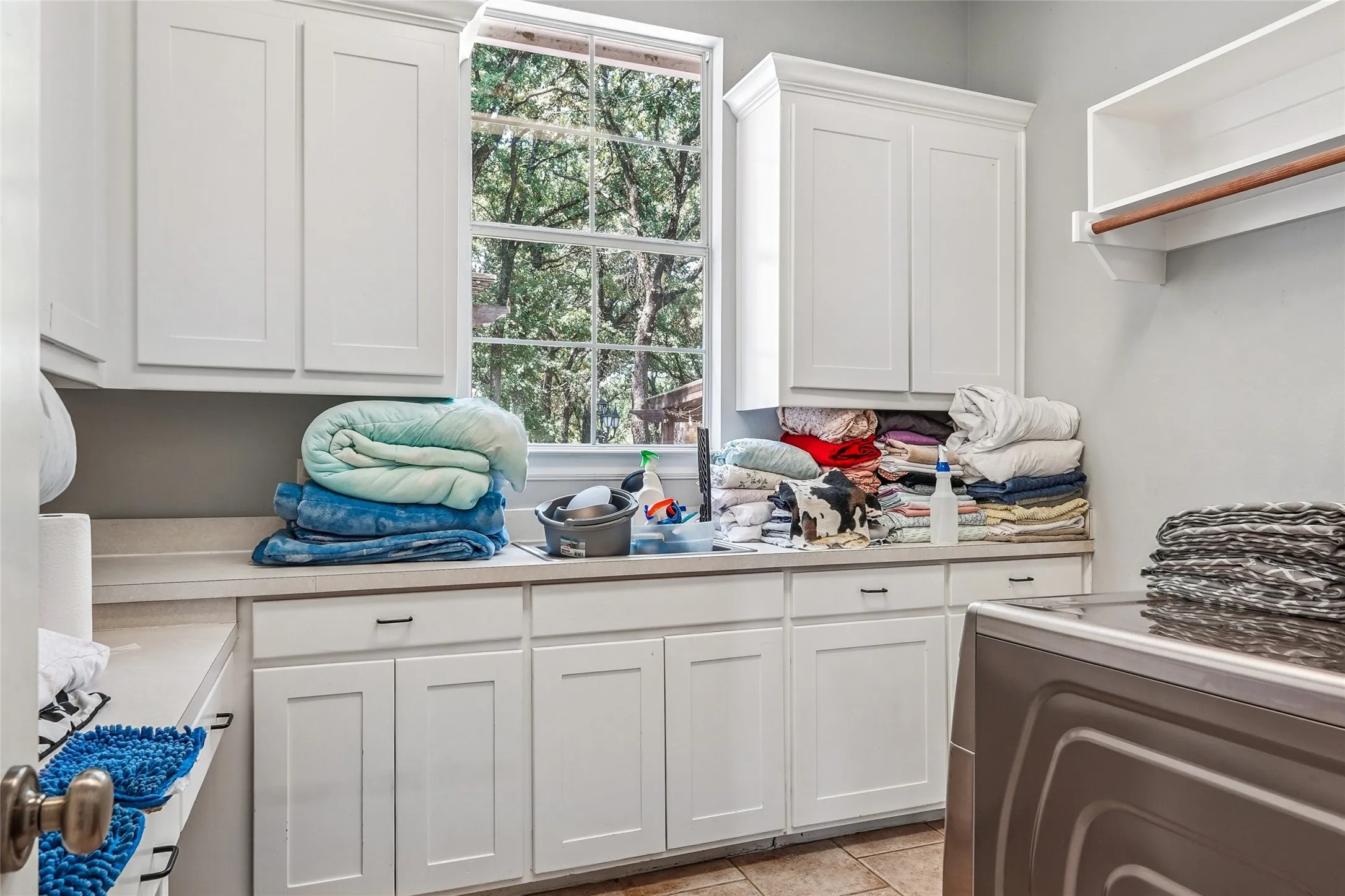 Utility room featuring extensive countertop space, white cabinetry with crown molding, a built-in hanging rod, and tile flooring