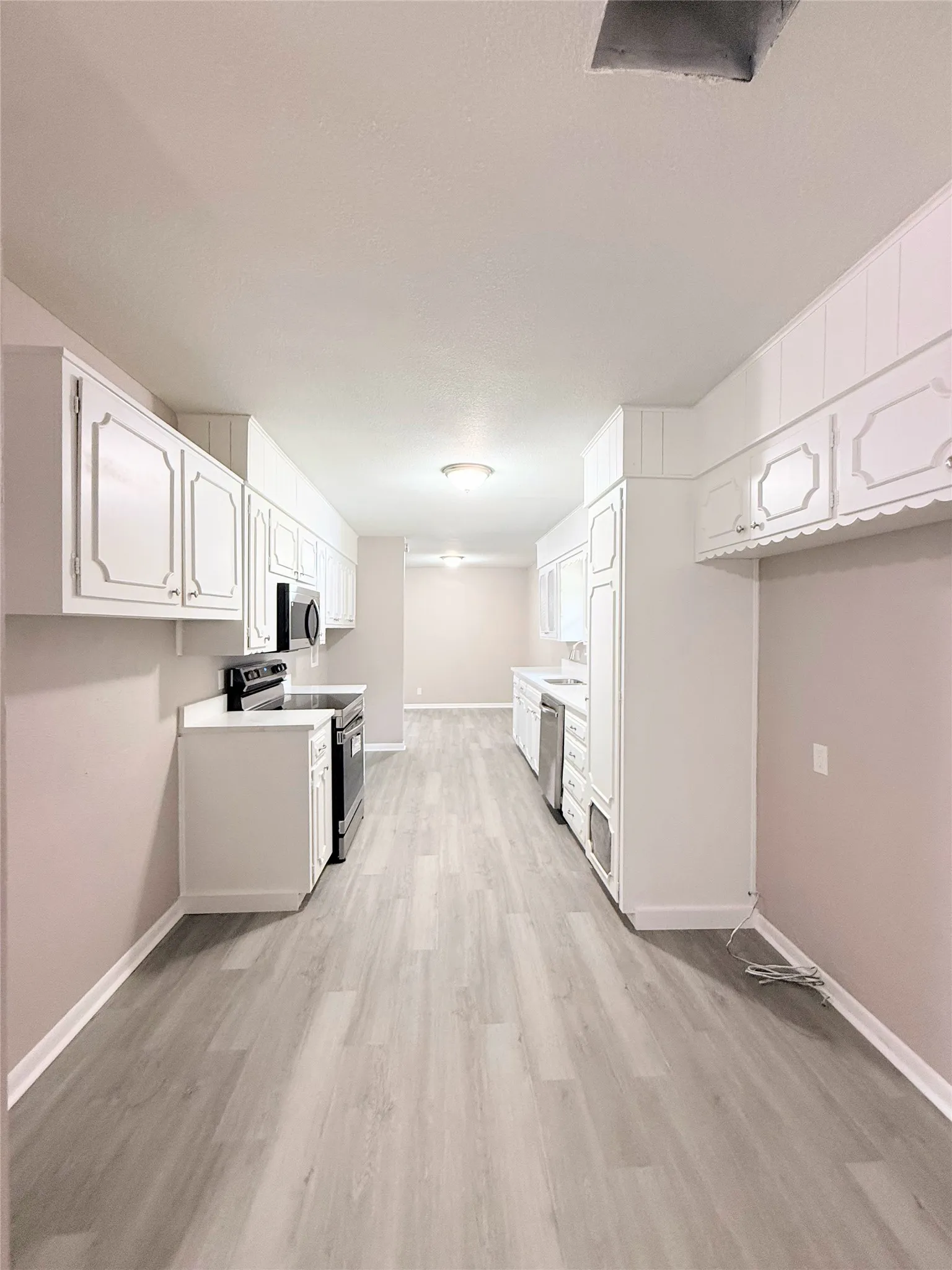 Kitchen featuring light wood-finish flooring, white cabinetry, a black oven, and a built-in dishwasher