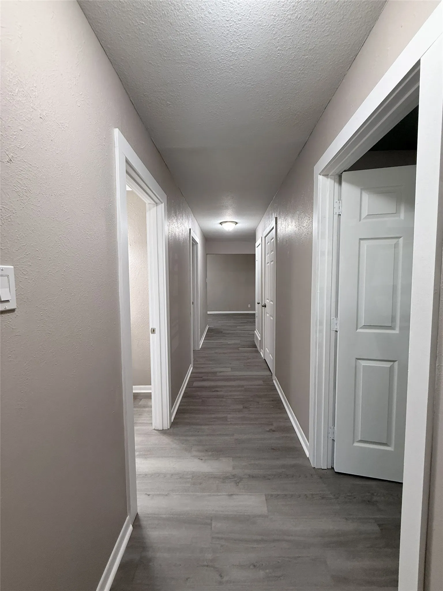 Hallway featuring wood-finish flooring, neutral wall paint, white trim, and multiple doorways