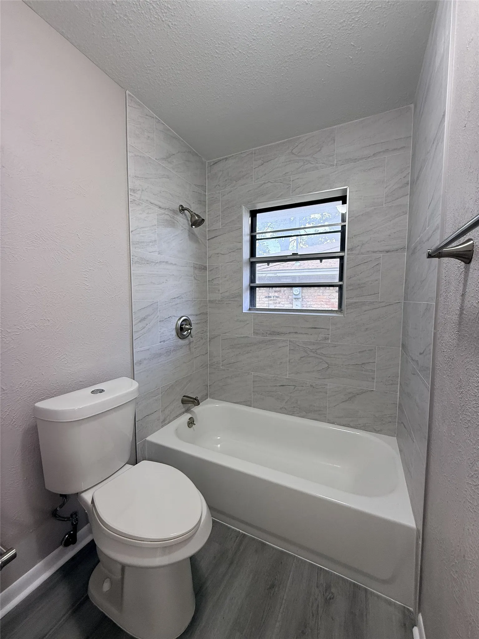 Bathroom featuring a white bathtub, light-toned wall tile surround, window with privacy screen, chrome fixtures, and wood-finish flooring