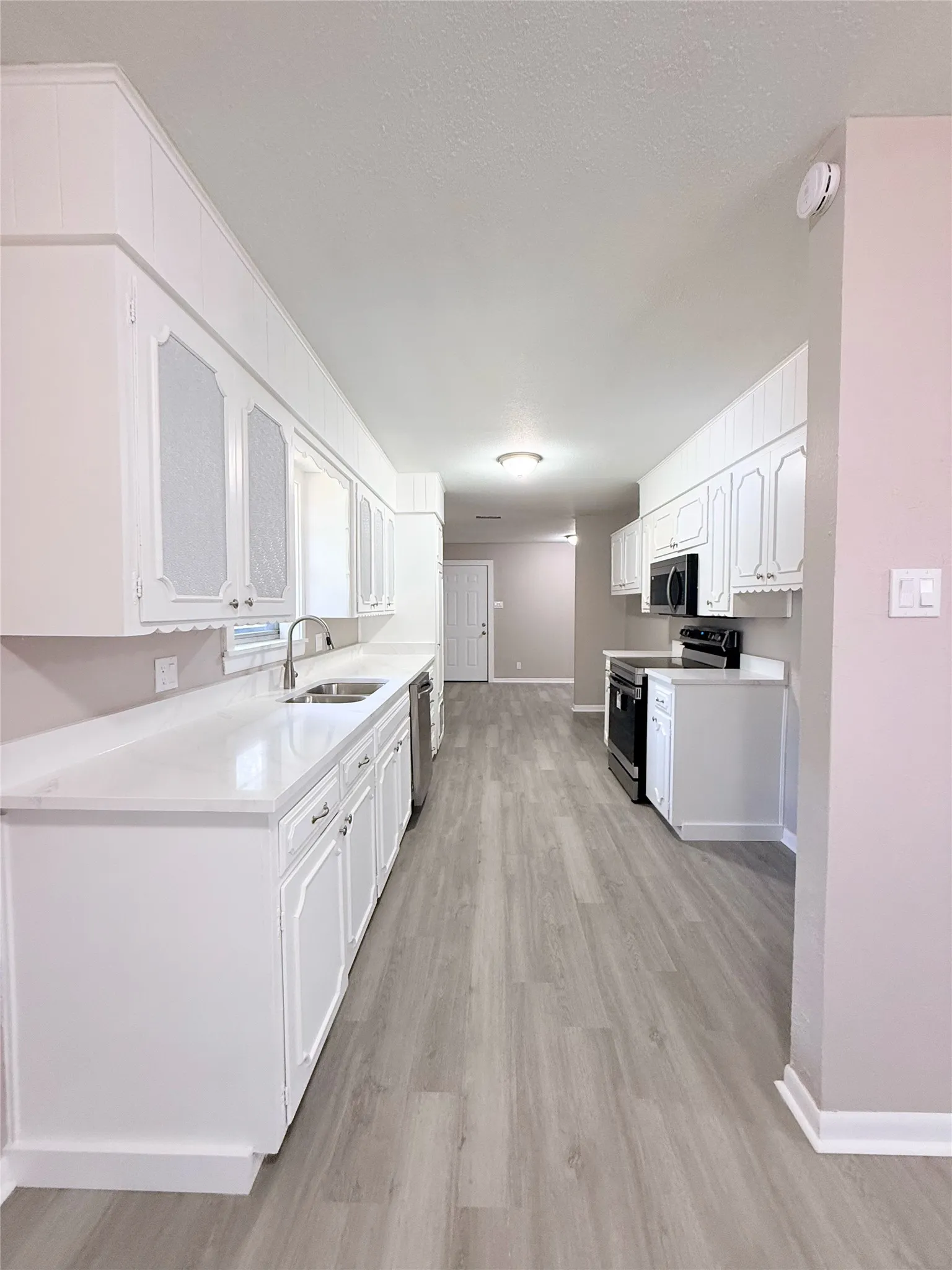 Galley kitchen featuring white cabinetry, light-toned countertops, and wood-finish flooring