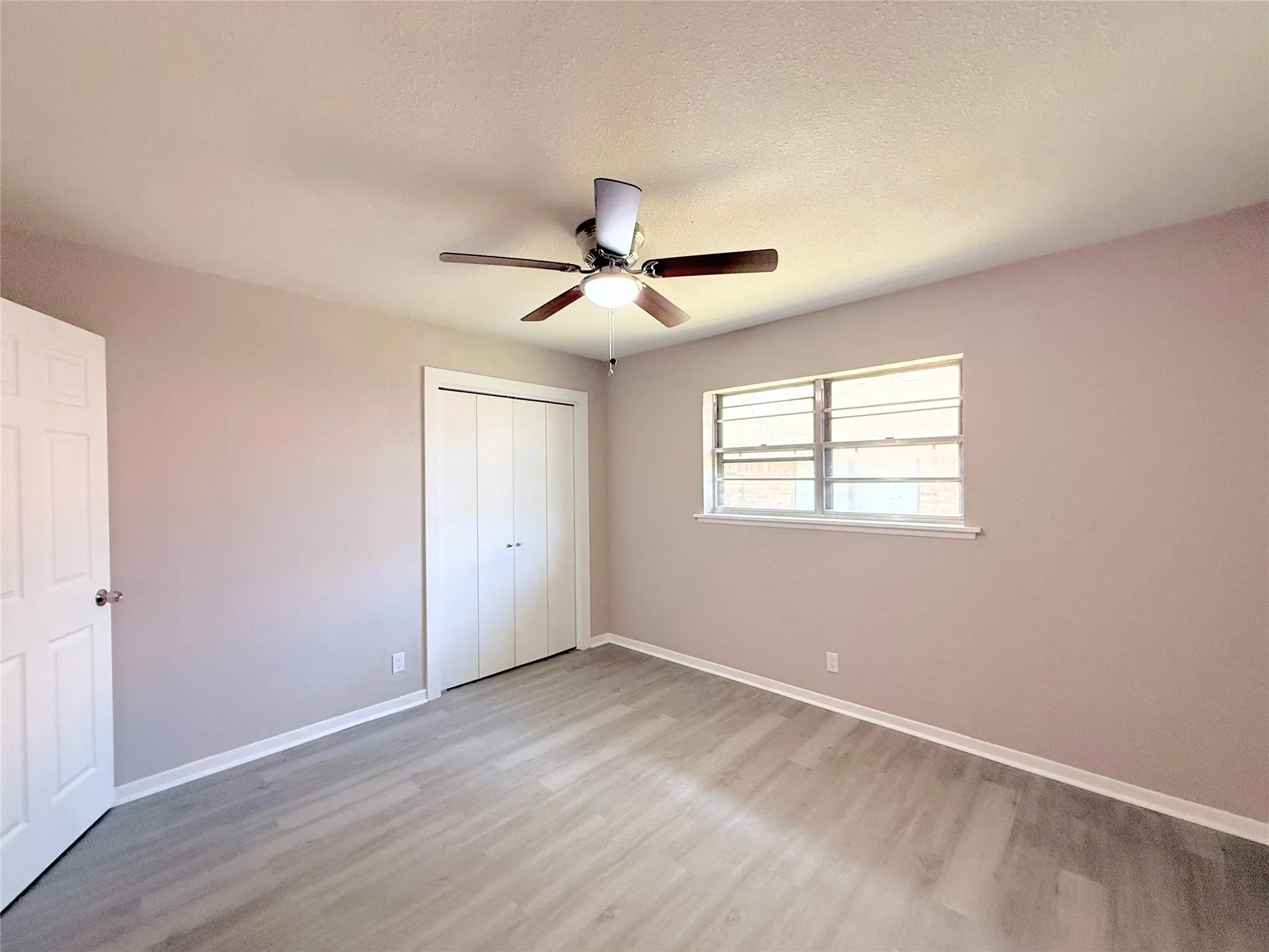 Room featuring wood-finish flooring, a ceiling fan with integrated lighting, a window with horizontal blinds, and a bi-fold closet