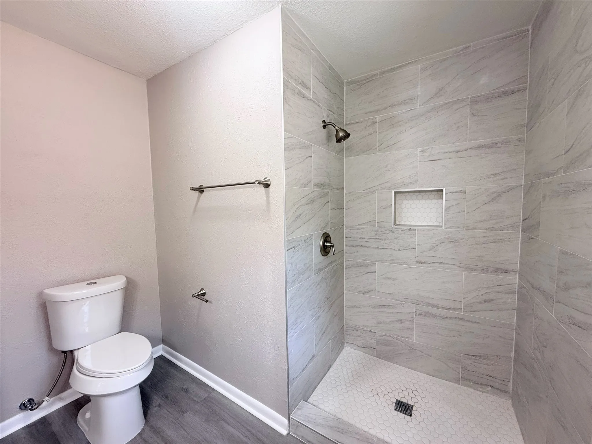 Walk-in shower featuring large format tile walls, a built-in niche with hexagonal mosaic tile, and a hexagonal mosaic tile shower pan