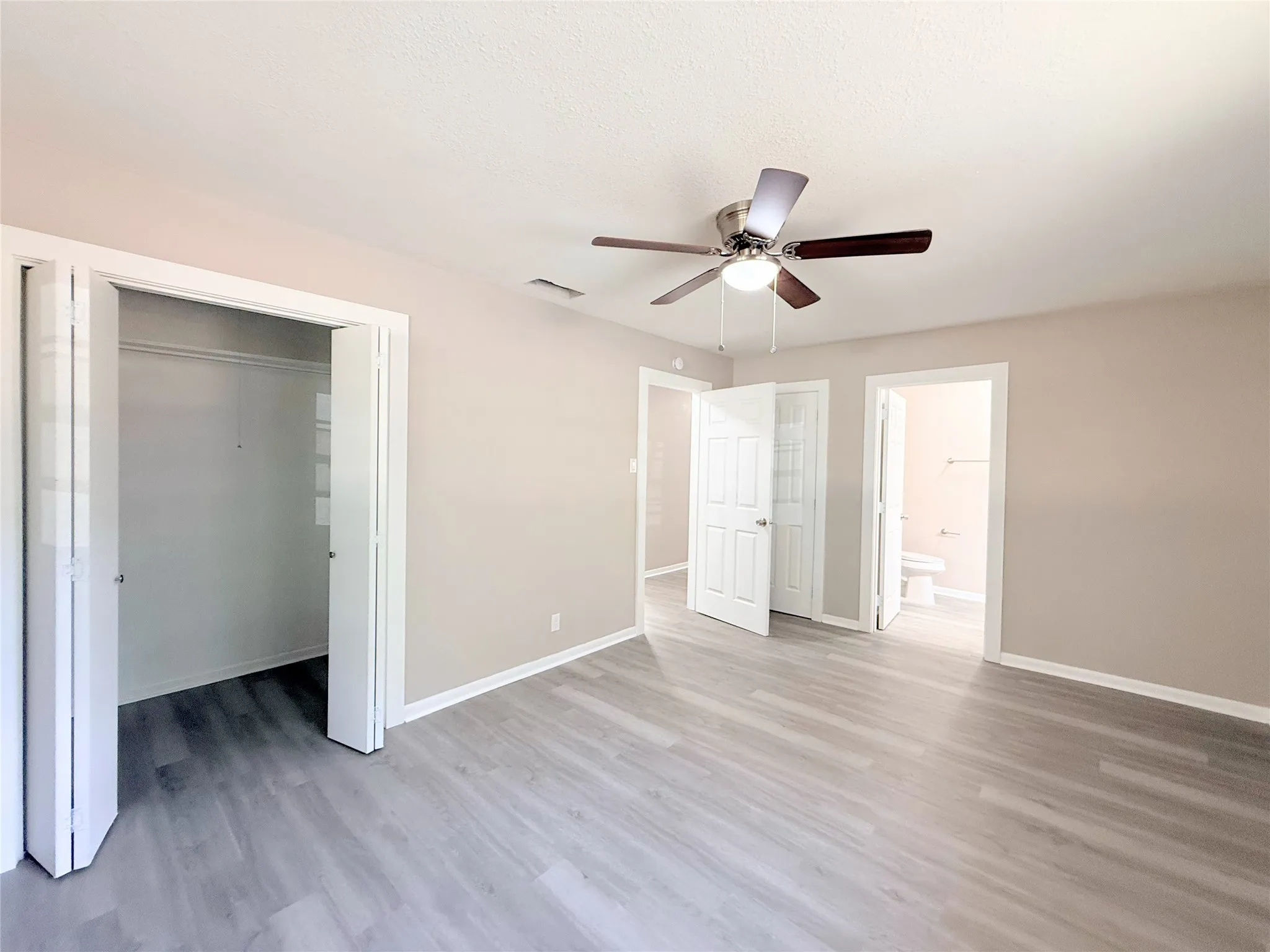 Spacious room featuring wood-finish flooring, a contemporary ceiling fan with integrated lighting, and neutral wall tones