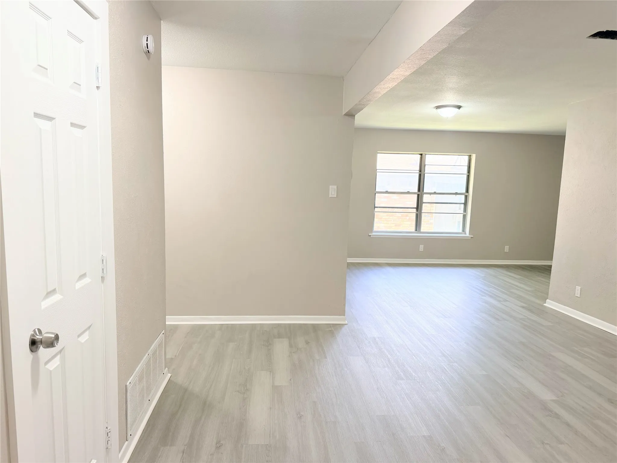 Interior doorway with a satin nickel doorknob, grey wood-finish flooring, neutral wall paint, white baseboards, and a large window providing natural light