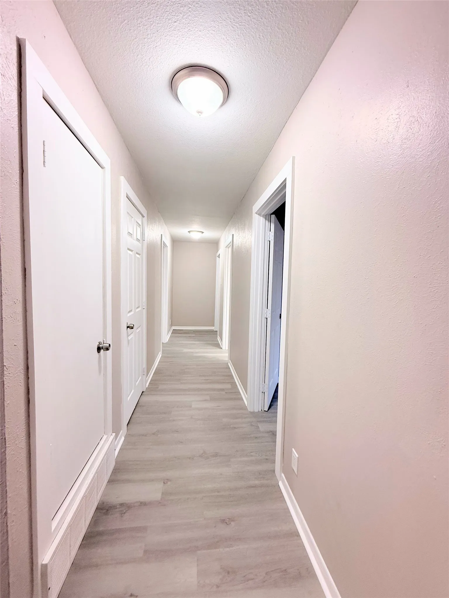 Hallway featuring wood-finish flooring, light neutral wall tones, white trim, and flush-mount ceiling lighting