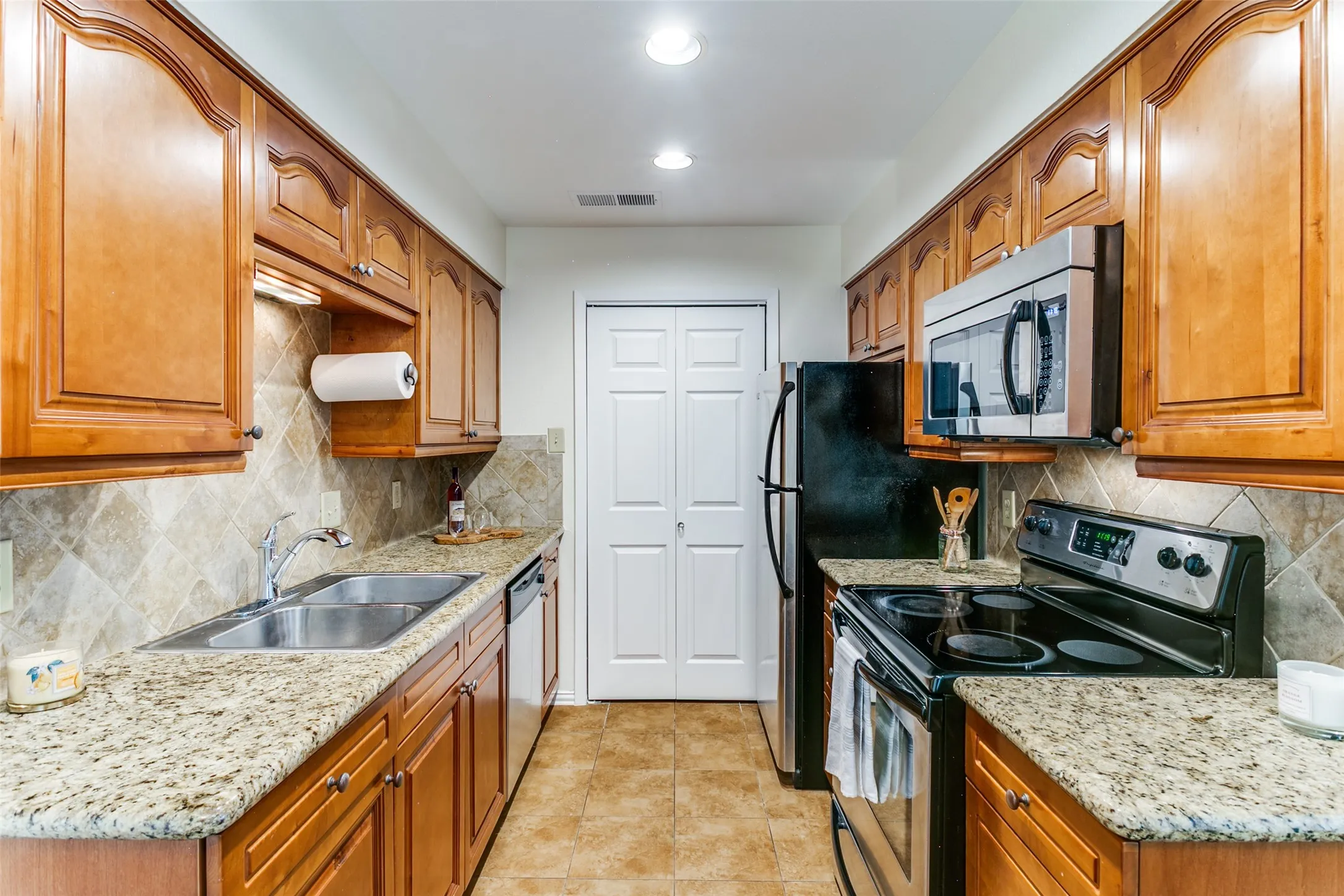 The kitchen has granite countertops, stainless appliances and a refrigerator. The doors to the full size laundry room are at the end.